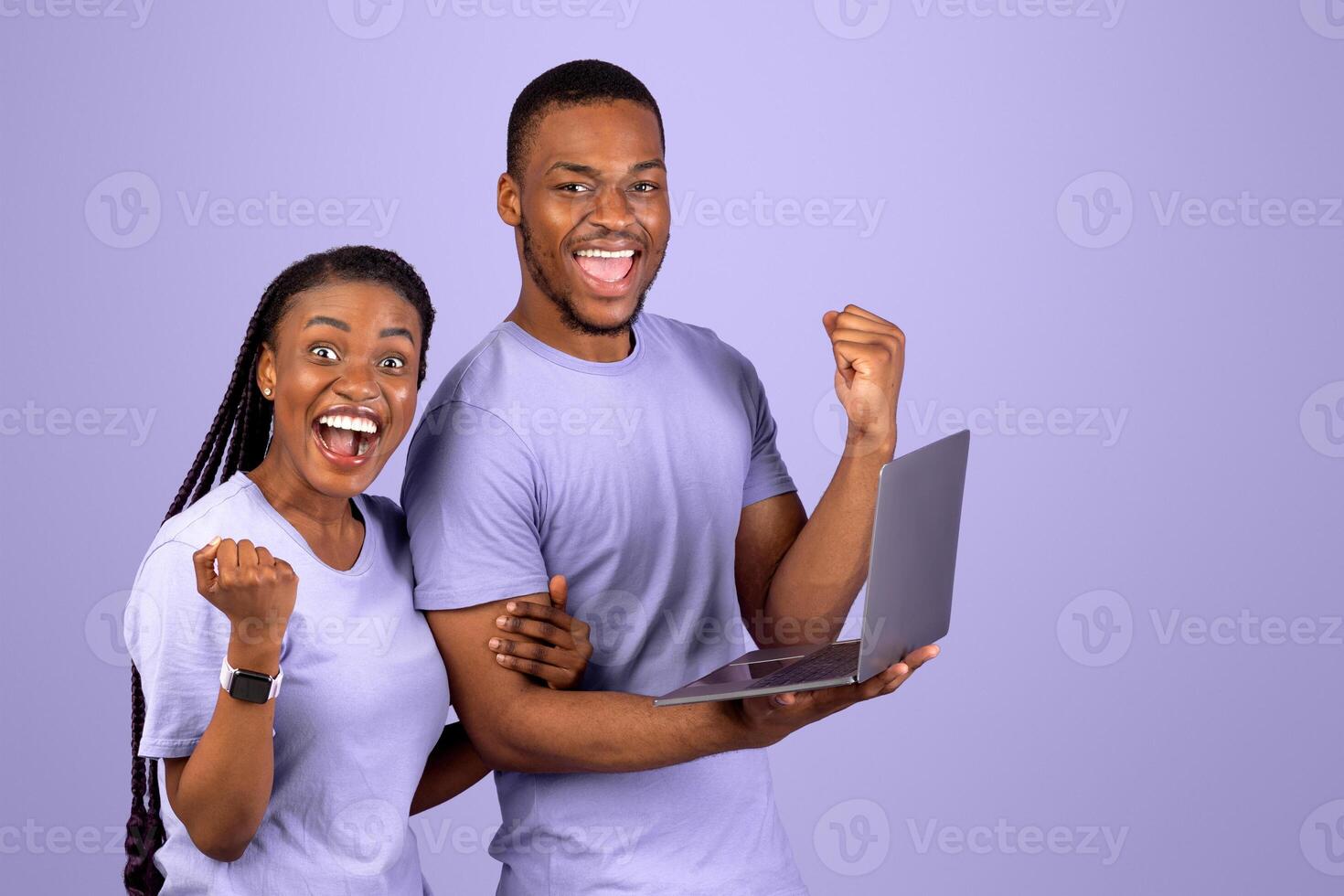 Yeah. Portrait of excited black couple celebrating online win, great deal or business success, holding and using laptop computer, screaming and shaking clenched fists, looking at camera photo