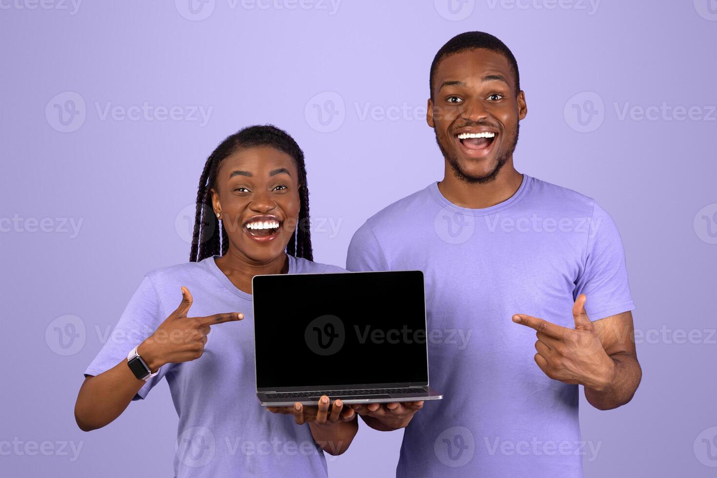 Cool Website. Happy African American Couple Pointing At Laptop With Black Blank Screen, Young Cheerful Guy And Lady Showing Copy Space For Online Advertisement, Posing Over Purple Violet Wall, Mock Up photo