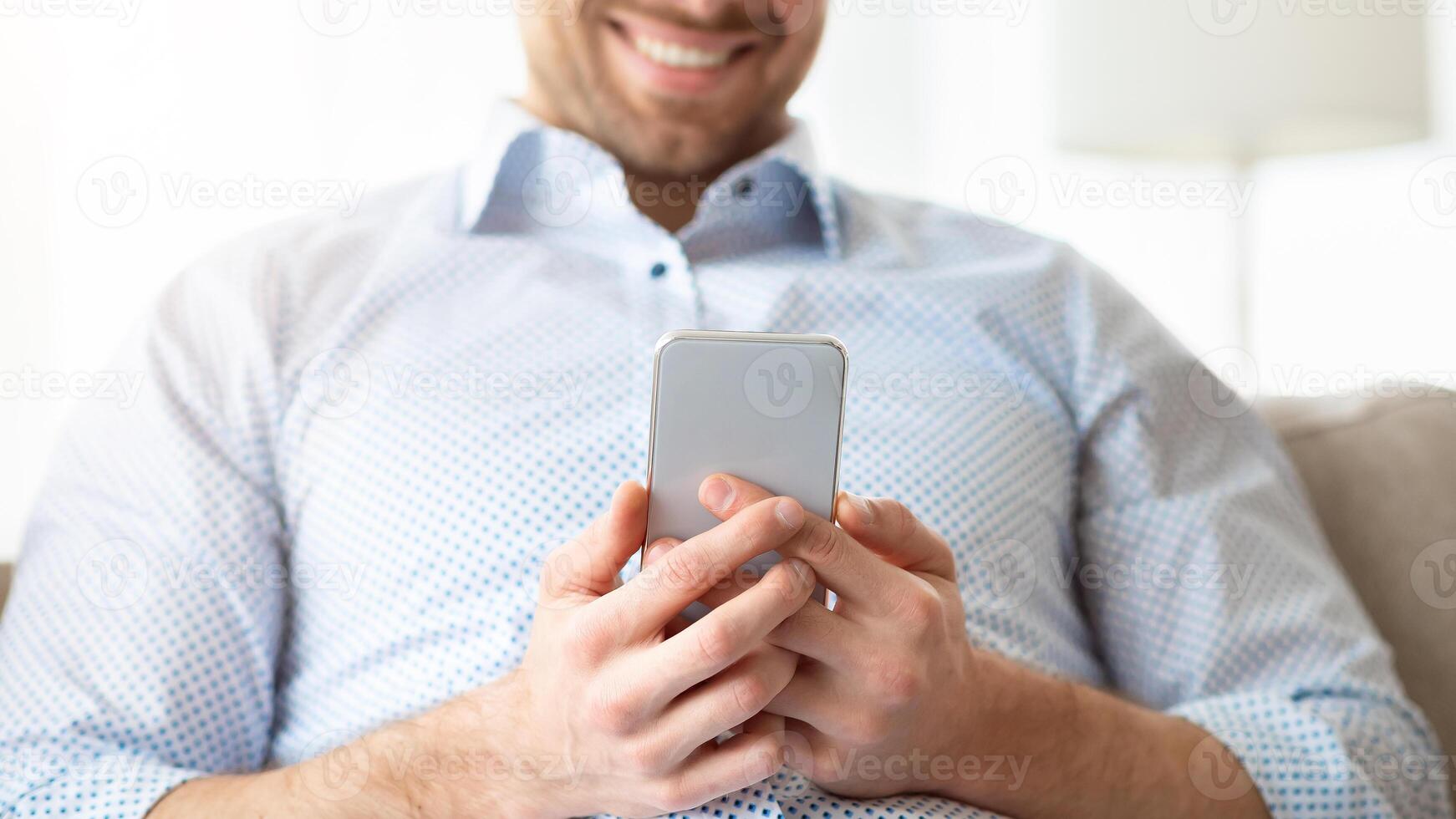 Browsing Internet. Cheerful handsome man using his smartphone sitting on the couch at home, copyspace photo