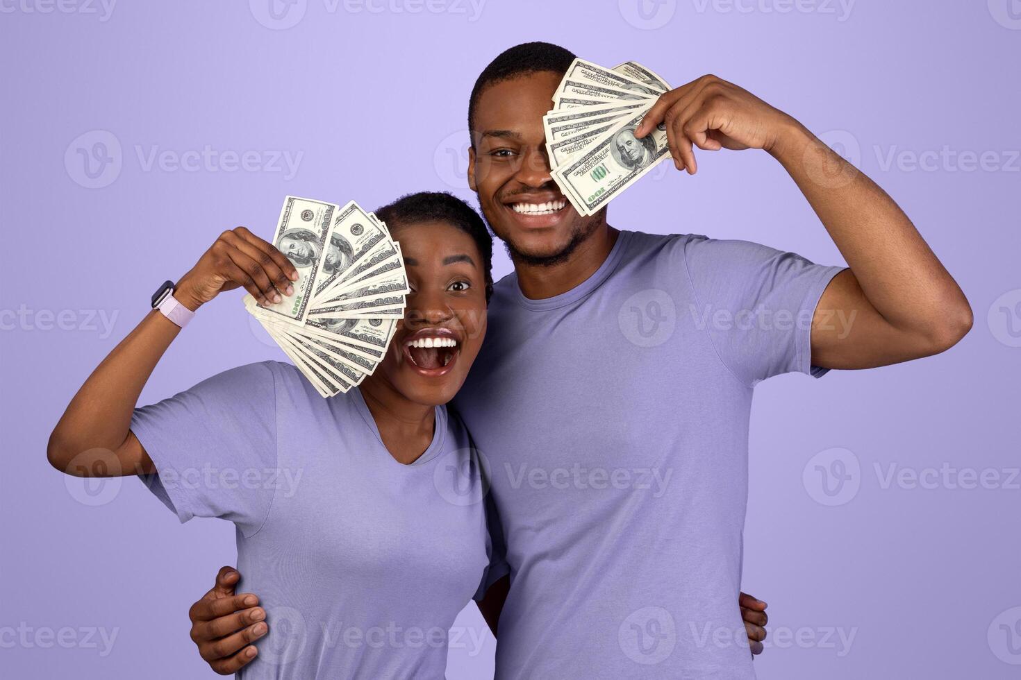 Joyful black man and woman won lottery, hugging and covering eye with bunch of money banknotes. Emotional lucky couple holding cash on purple violet studio background wall. Gambling, Loan Concept photo