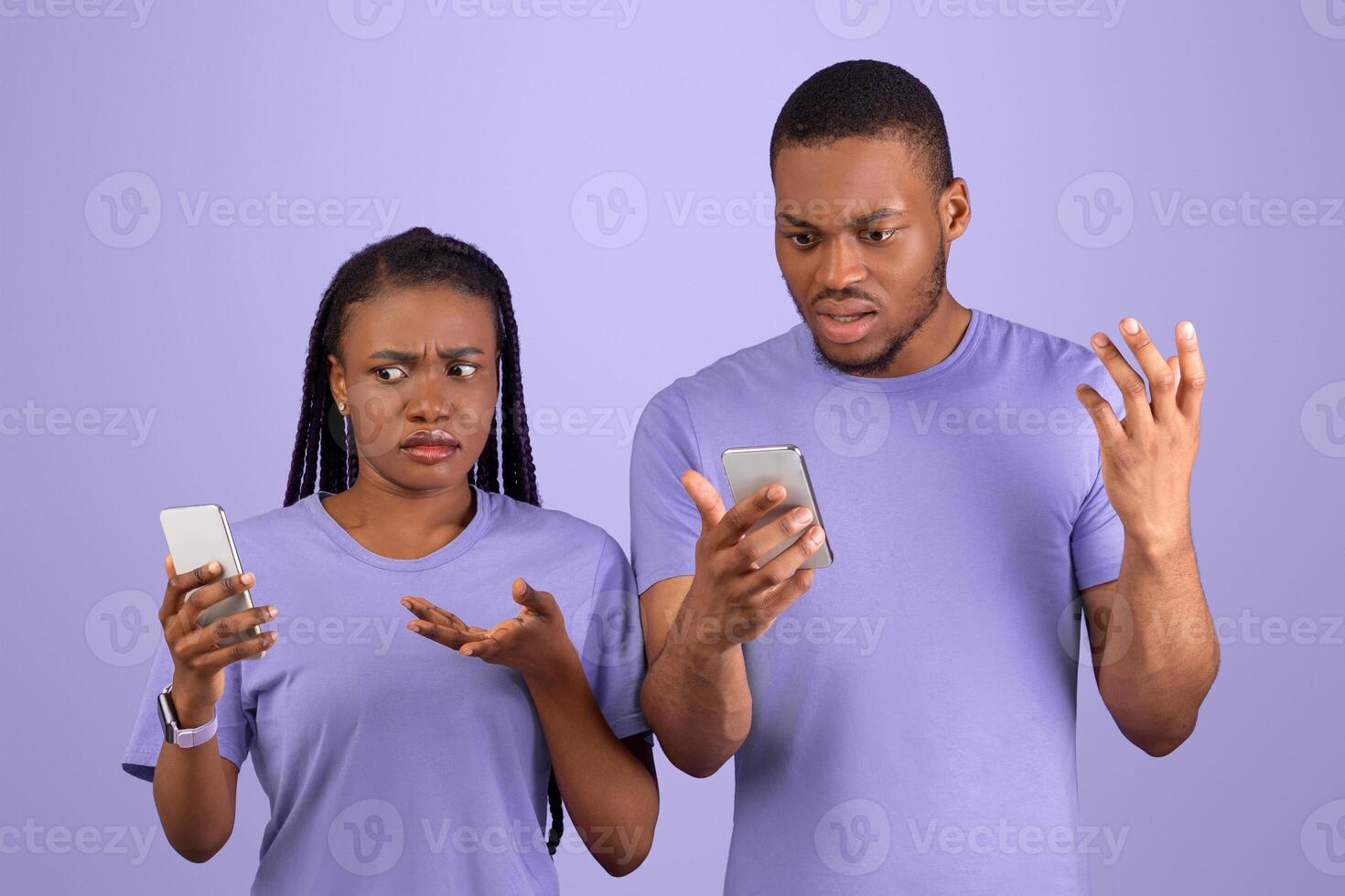 Strange Message, Bad News, Internet Connection Problem. Confused sad millennial African American couple looking at their phones and shrugging shoulders, standing isolated on purple violet background photo