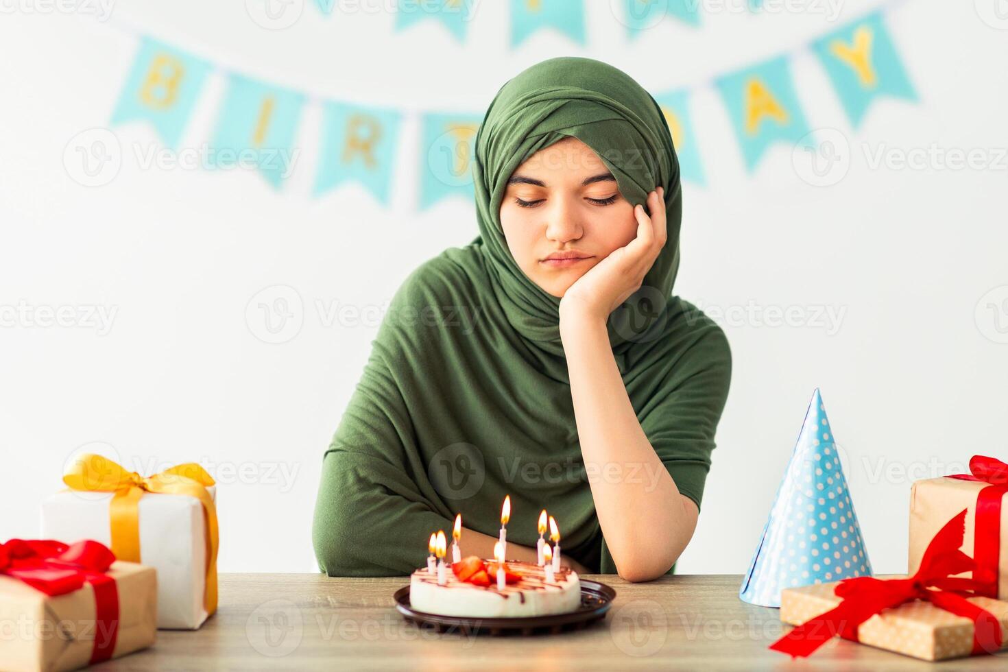 Sad Indian teen girl in hijab having dull birthday party, feeling bored, celebrating holiday alone during coronavirus isolation. Unhappy Muslim teenager disliking lonely b-day celebration at home photo