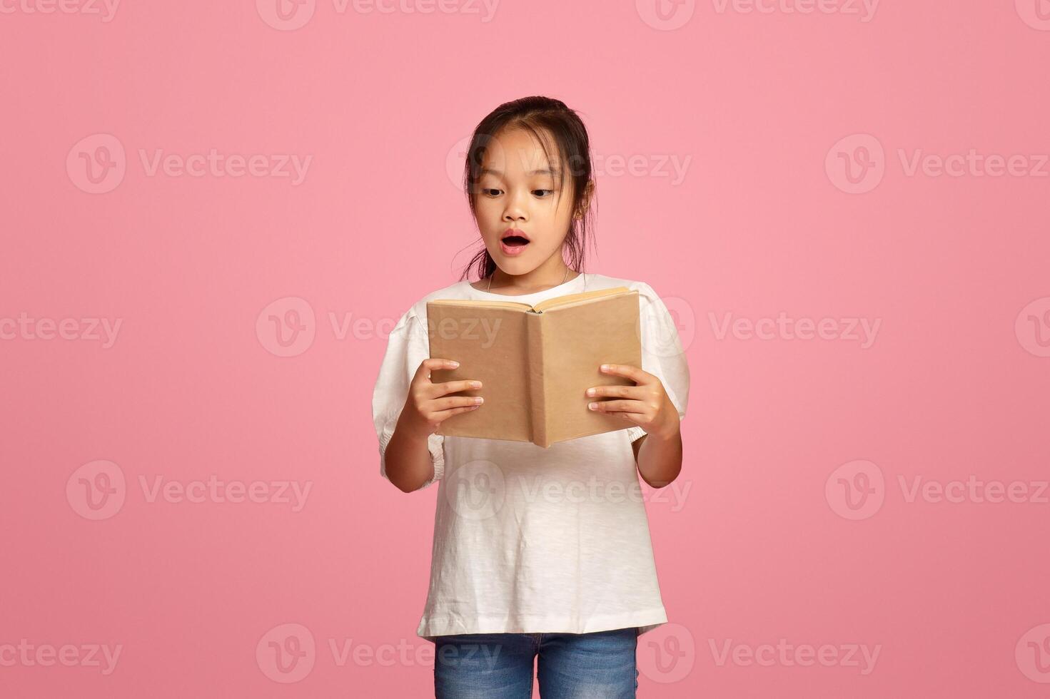 Focused diverse schoolkids reading books on pink background photo
