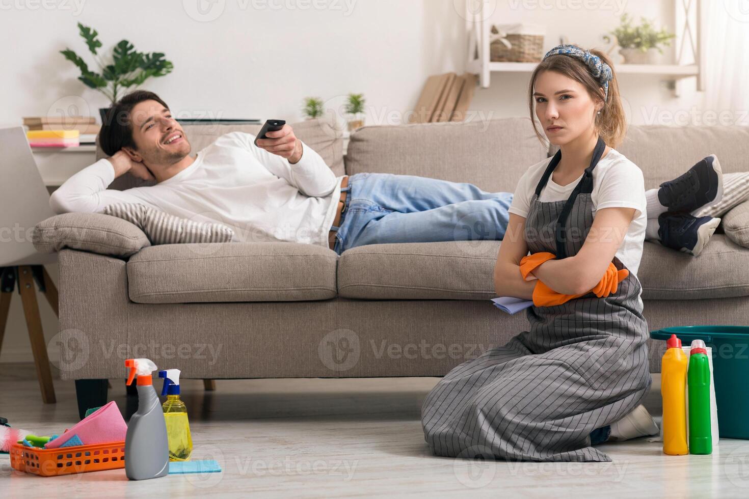 Household Chores Problem. Offended Woman Tired After Cleaning Sitting Next To Lazy Husband Relaxing On Couch photo