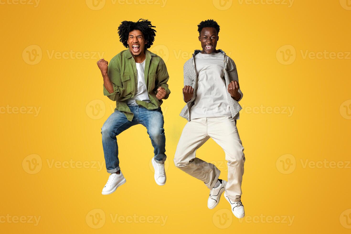 Big Joy. Two Happy Excited Black Guys Jumping In Air And Celebrating Success, Overjoyed Millennial African American Friends Emotionally Reacting To Win, Having Fun Over Beige Background, Full Length photo