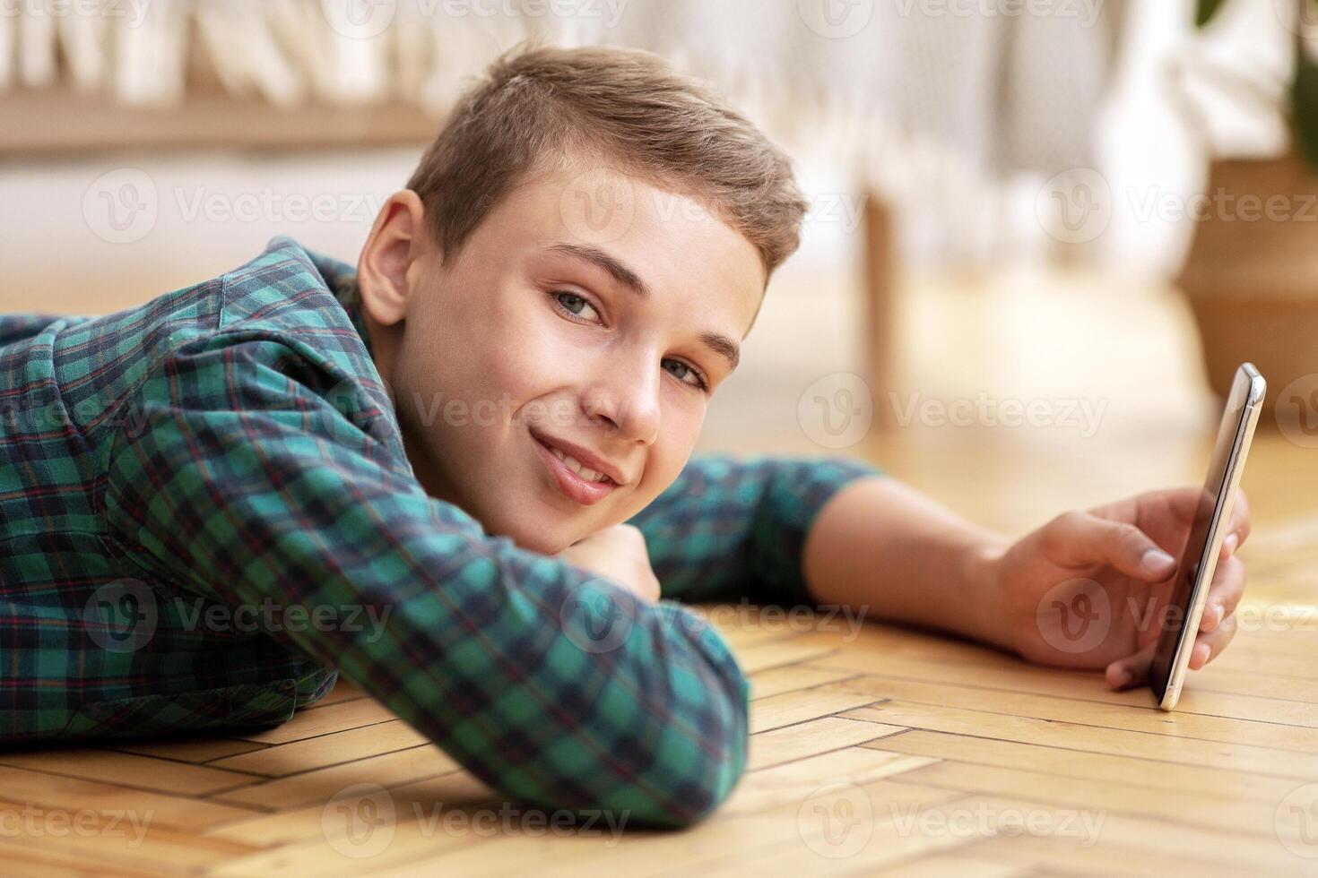 Smiling teenager laying on floor at home, using mobile phone, side view photo