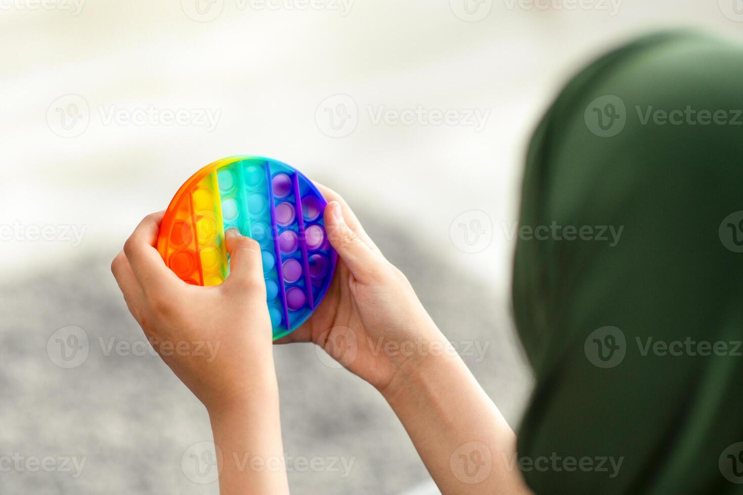 Cropped view of Muslim teenage girl in hijab playing with antistress POP IT toy at home, closeup of hands. Unrecognizable youth in headscarf using sensory plaything to relieve stress, copy space photo
