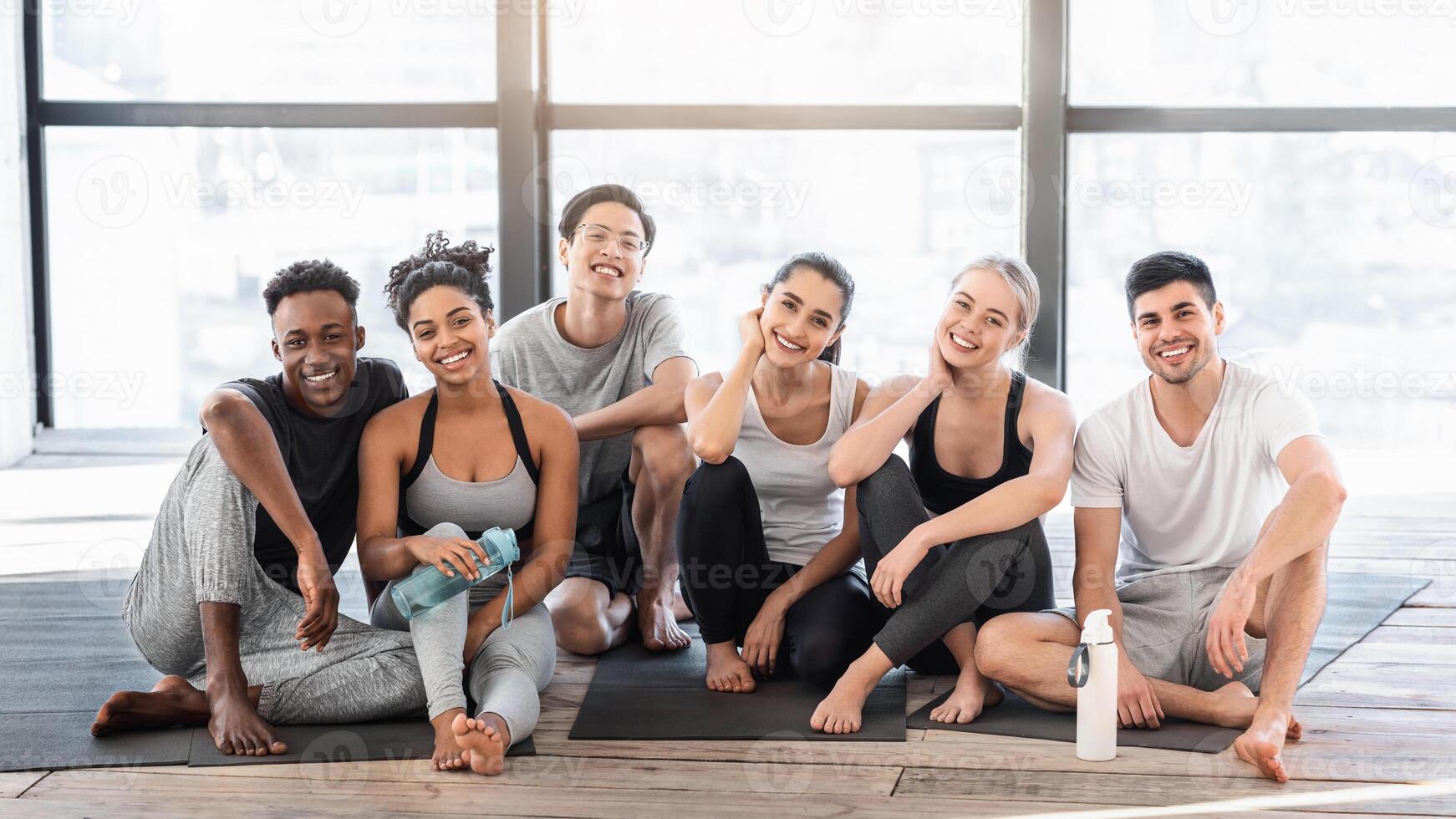 Happy sporty people posing in fitness studio after yoga training, sitting on mats and smiling, enjoying healthy lifestyle photo