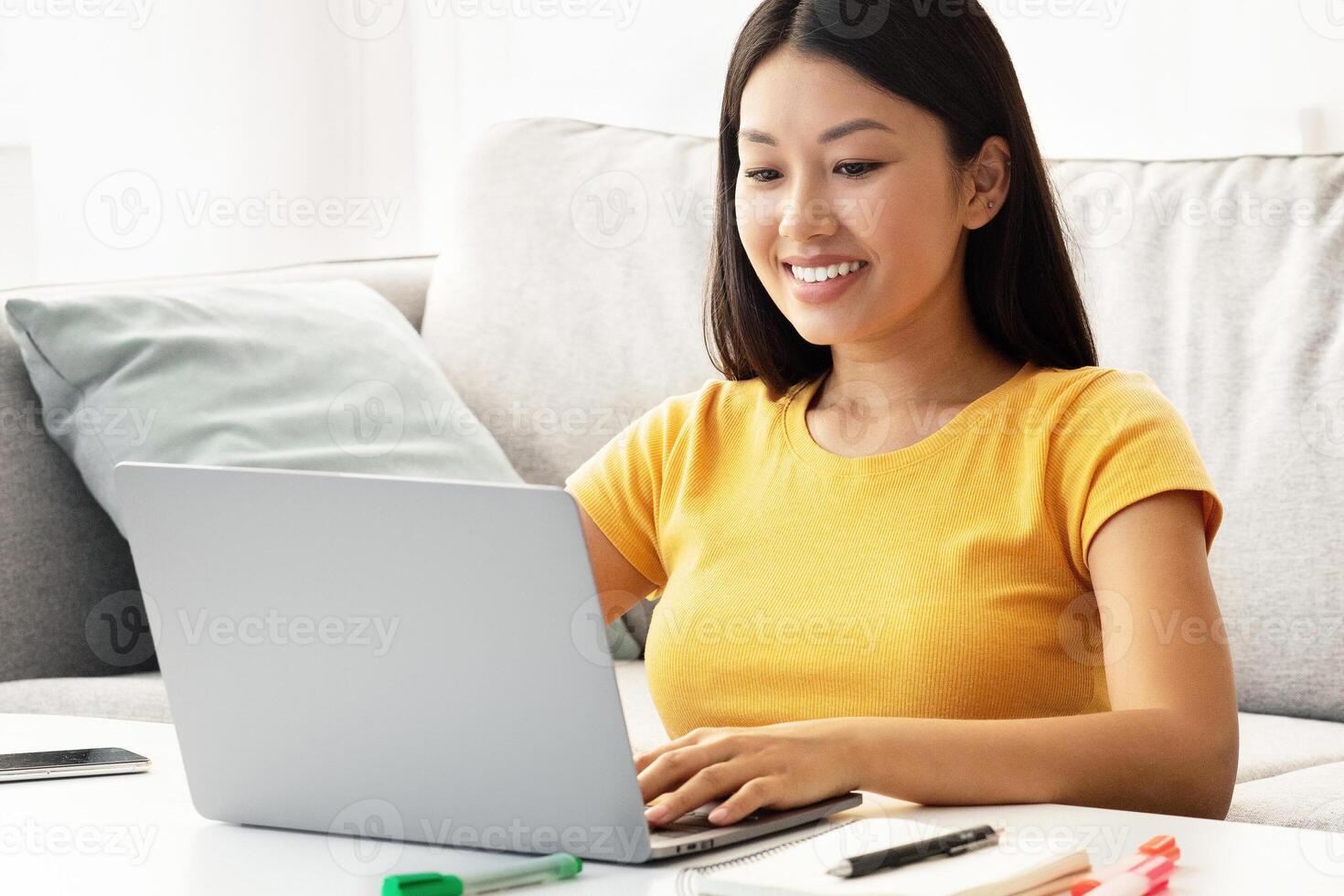Cheerful young japanese lady surfing on Internet, using laptop at home, cute puppy sitting by. Happy woman spending time with jack russel terrier dog, working online, typing on notebook keyboard photo
