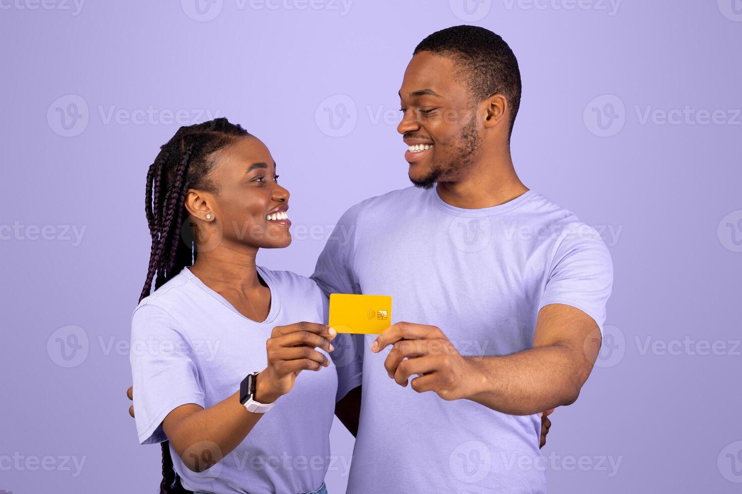 Happy Black Couple Hugging, Holding And Showing Golden Credit Card To Camera, Looking At Each Other, Recommending Banking Service Over Purple Violet Studio Background, Free Copy Space photo
