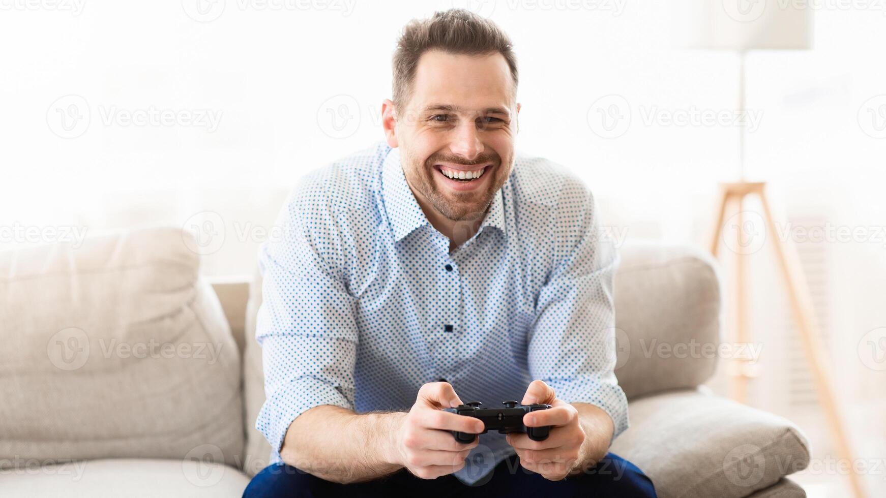 Young man playing games at home. Happy guy sitting on couch with joystick in hands, copy space photo