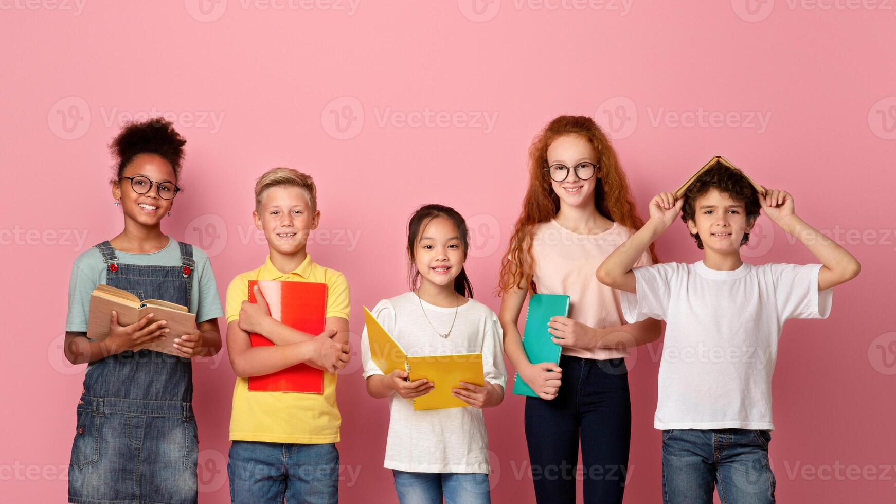 Multinational group of kids with books and notebooks ready for school over pink studio background photo