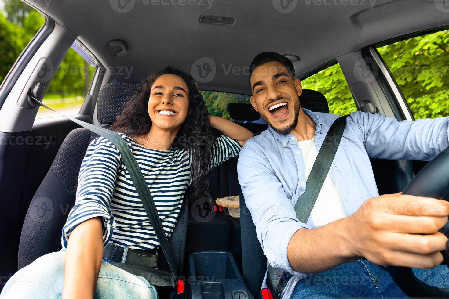 Emotional millennial couple enjoying journey by auto, shot from automobile dashboard, copy space. Excited middle-eastern guy and his pretty girlfriend going summer vacation by car photo