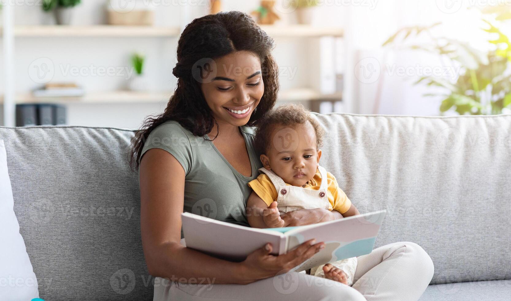 Portrait Of Caring Mom Reading Book To Cute Little Baby While They Relaxing On Couch At Home Together, Closeup Shot Of Loving African American Mother Bonding With Her Infant Child, Copy Space photo