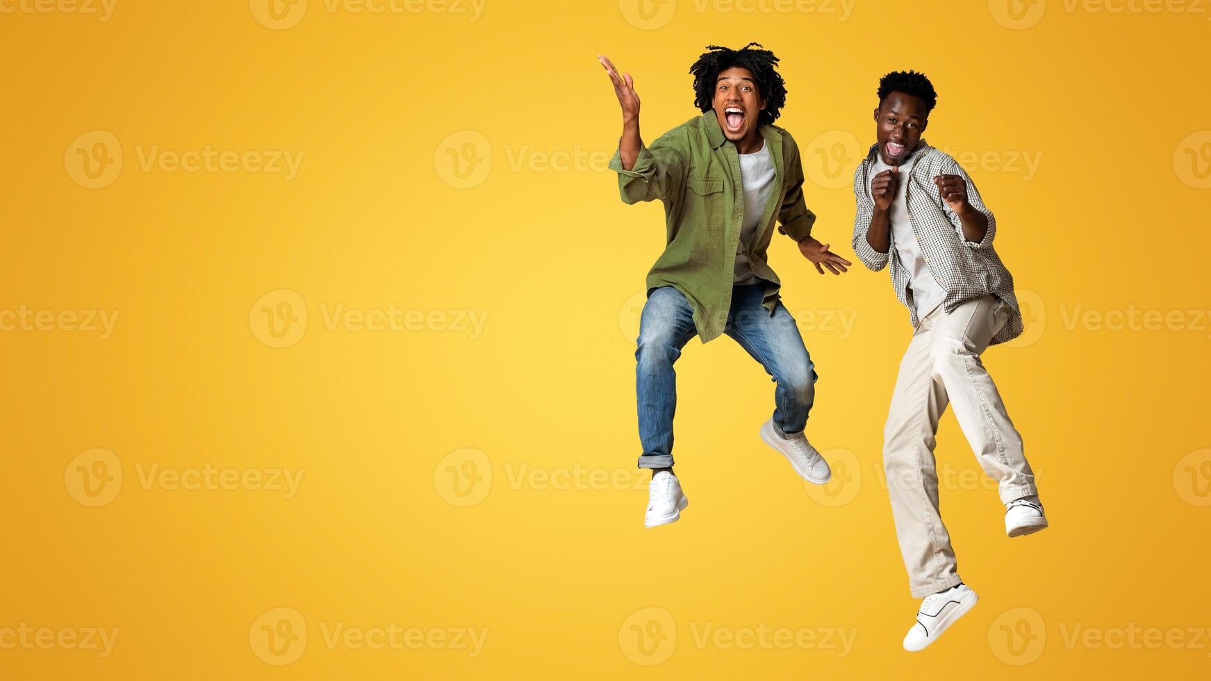 Crazy Mood. Two Overjoyed Black Guys Jumping Over Beige Studio Background, Full Length Shot Of Happy Emotional African American Male Friends In Casual Clothes Having Fun Together, Copy Space photo