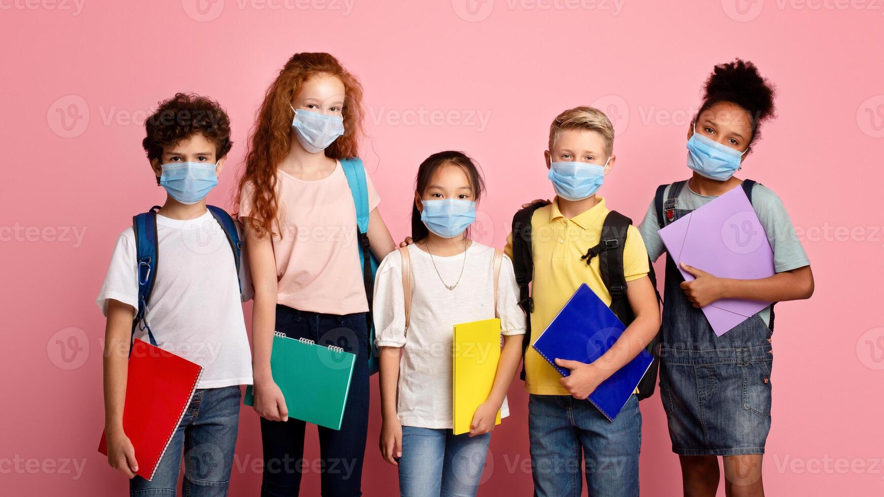 Health care and education concept. Portrait of schoolchildren wearing protective masks against pink background photo