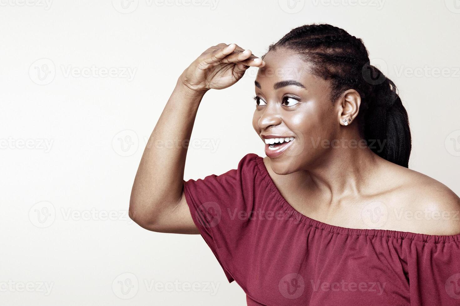 Curious african american young woman looking at something interesting or exciting, holding hand by forehead and looking at copy space for advertisement, beige studio background, panorama photo