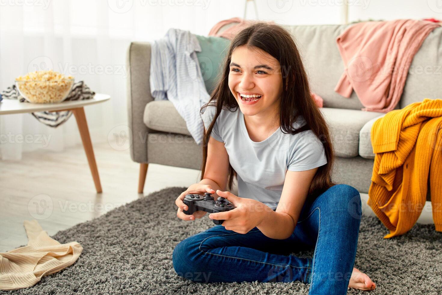 Happy Indian teenager with joystick playing online computer games in messy room during covid lockdown. Cheerful adolescent with controller engaged in gaming at home photo