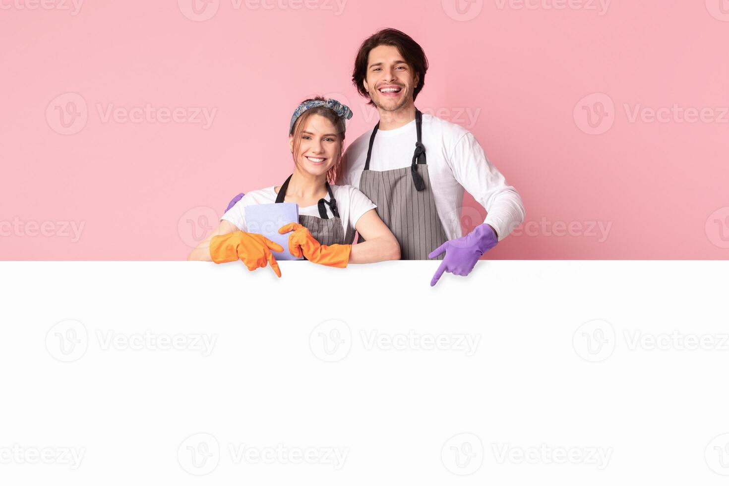 Domestic Housekeeping Service Ad. Smiling Man And Woman Wearing Gloves, Leaning And Pointing At White Advertisement Board With Copy Space photo