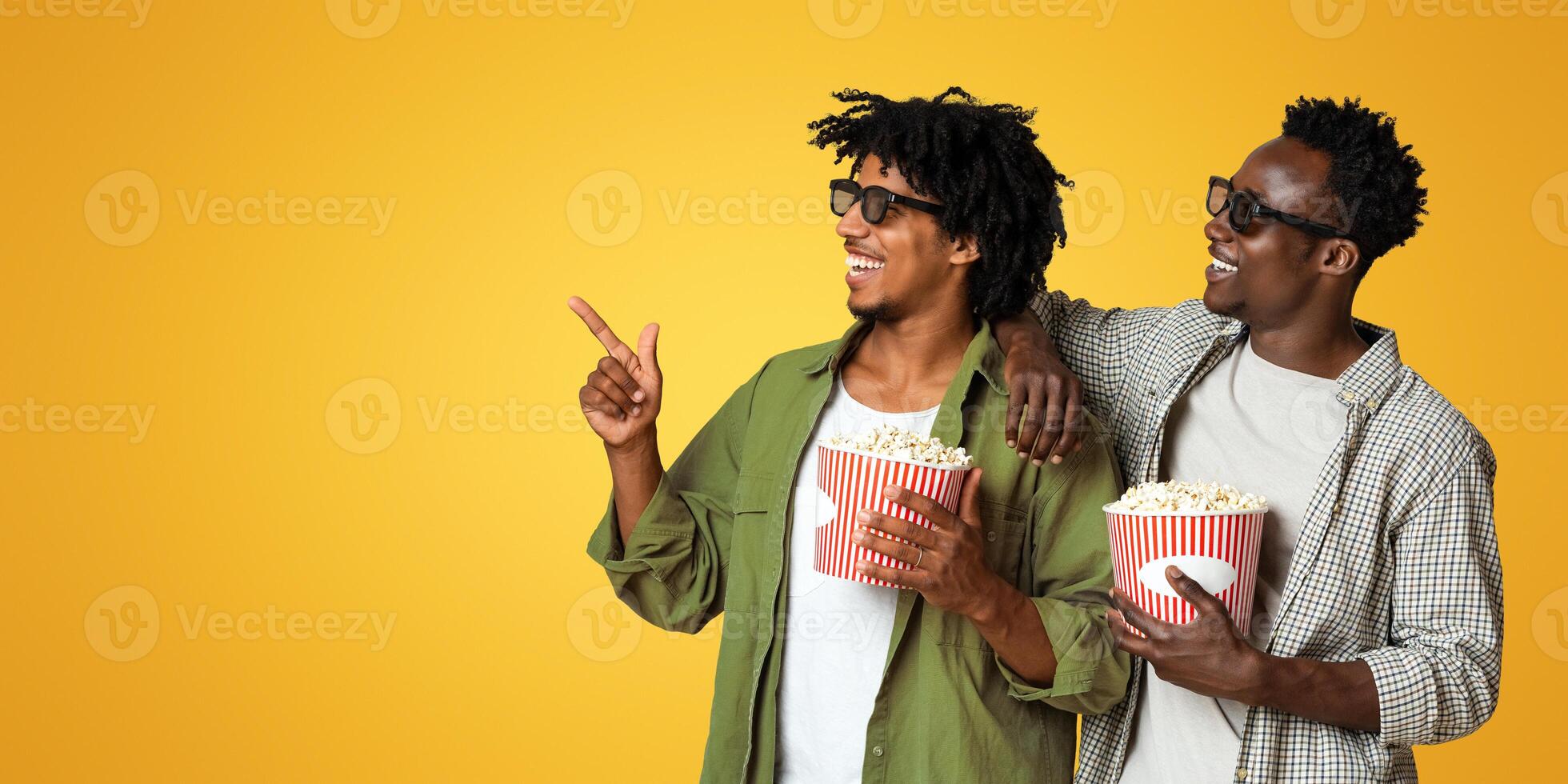 Cinema Ad. Two Black Friends With Popcorn Pointing Aside At Copy Space Over Beige Background, Happy African American Mates Wearing 3D Glasses Having Fun Together, Enjoying Movie Time, Panorama photo