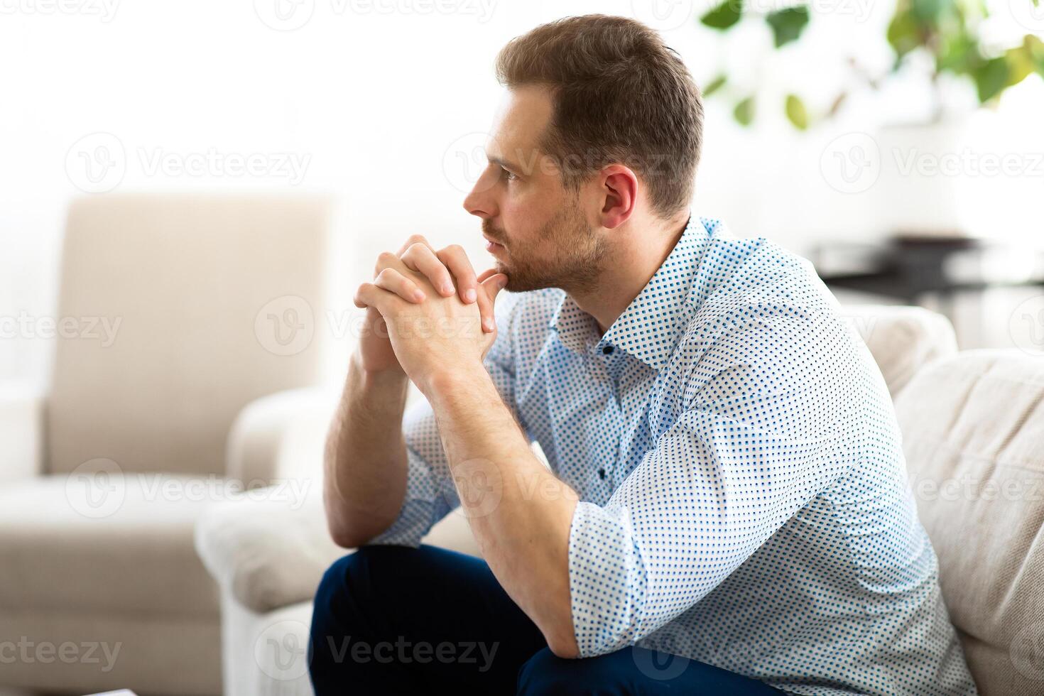 Side view portrait of pensive millennial man thinking, sitting on the couch, looking away, copy space photo