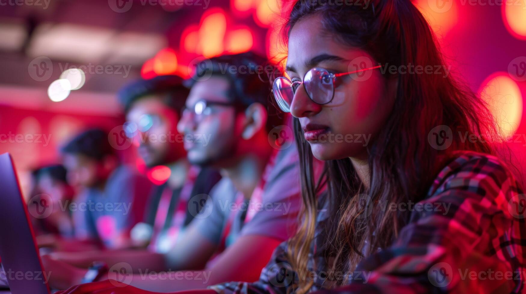 Participants focus intently on their laptops during a coding event, surrounded by dynamic lighting that creates an energetic and inspiring environment. photo