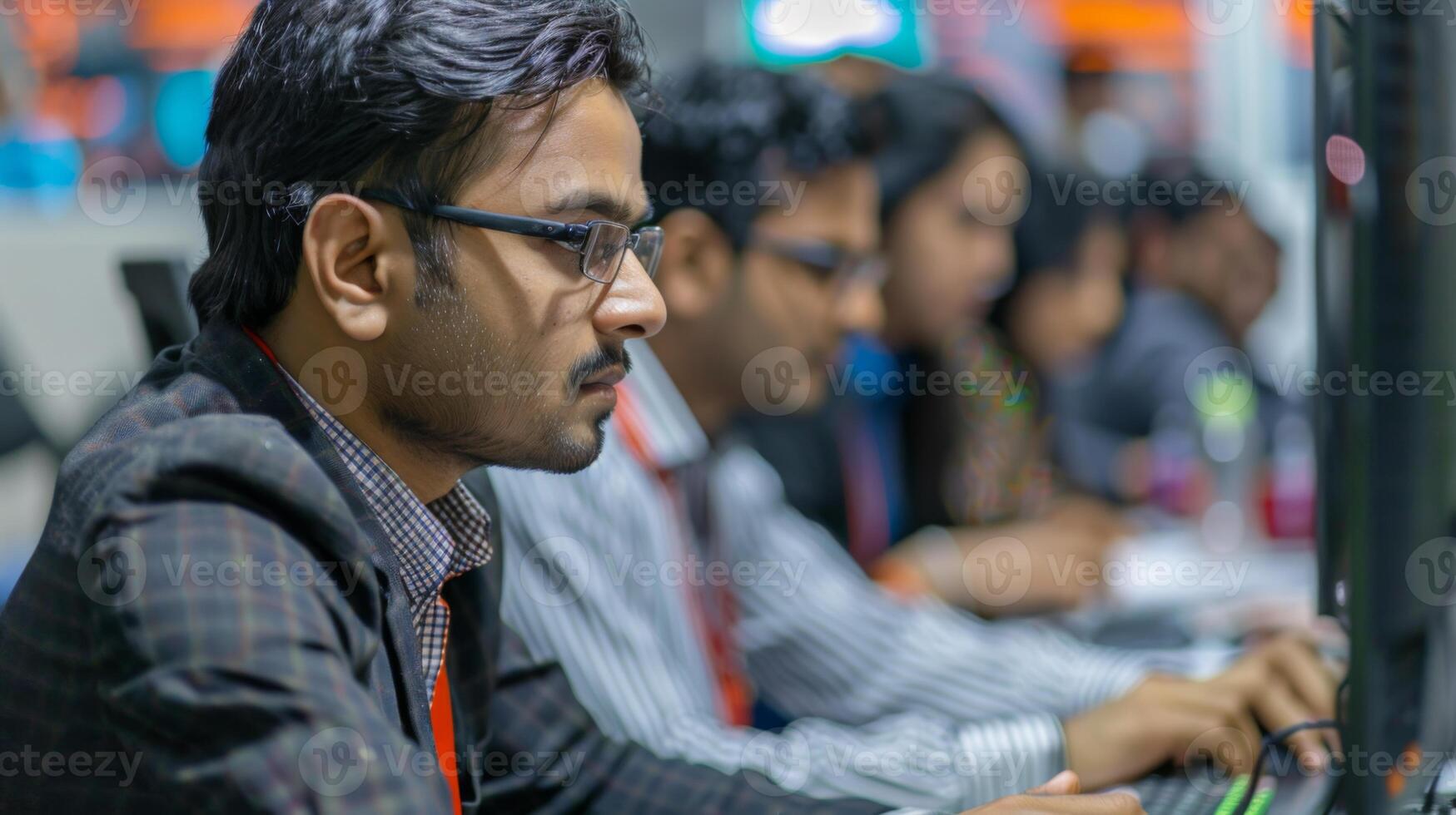 Several young adults concentrate on their computer screens in a vibrant office environment filled with technology. They are collaborating on various tasks. photo