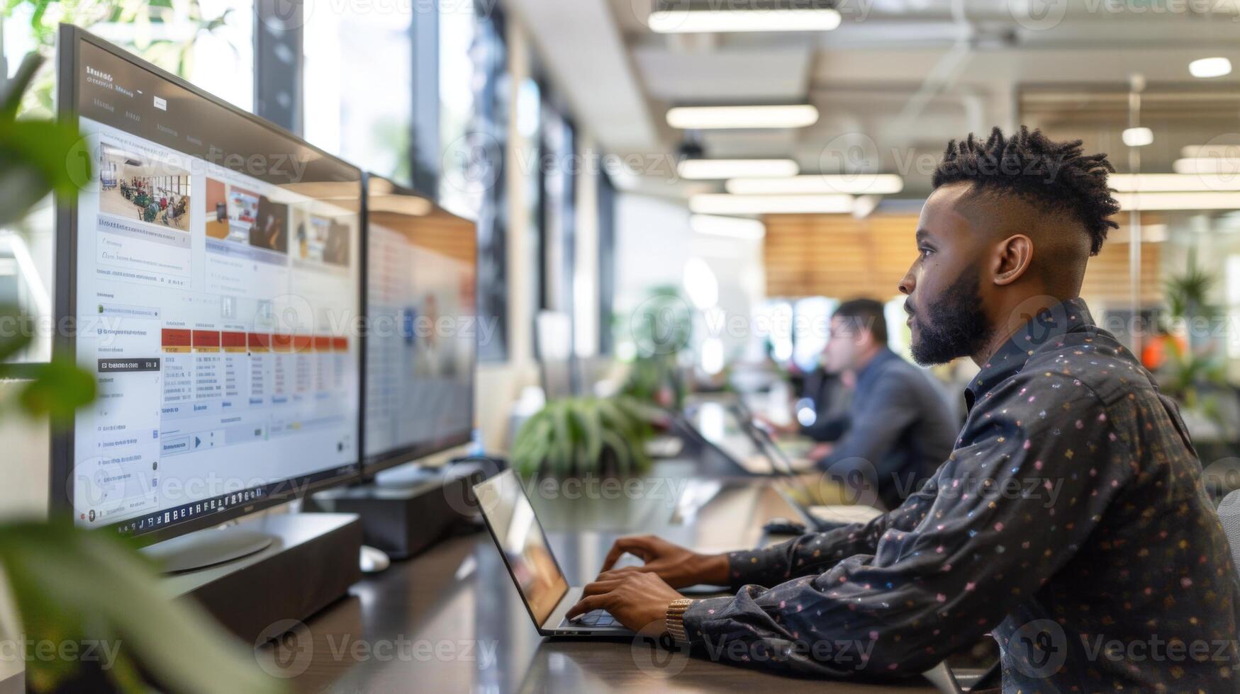 Focused individual uses laptop in a vibrant office filled with plants, engaged in work activities alongside colleagues at their desks during business hours. photo