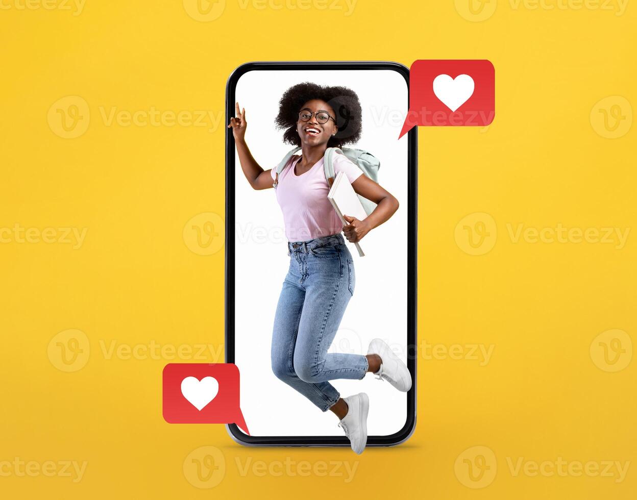 A joyful young woman with curly hair jumps from a large smartphone. She holds a backpack, showing enthusiasm for technology and connection through messaging and social media. photo