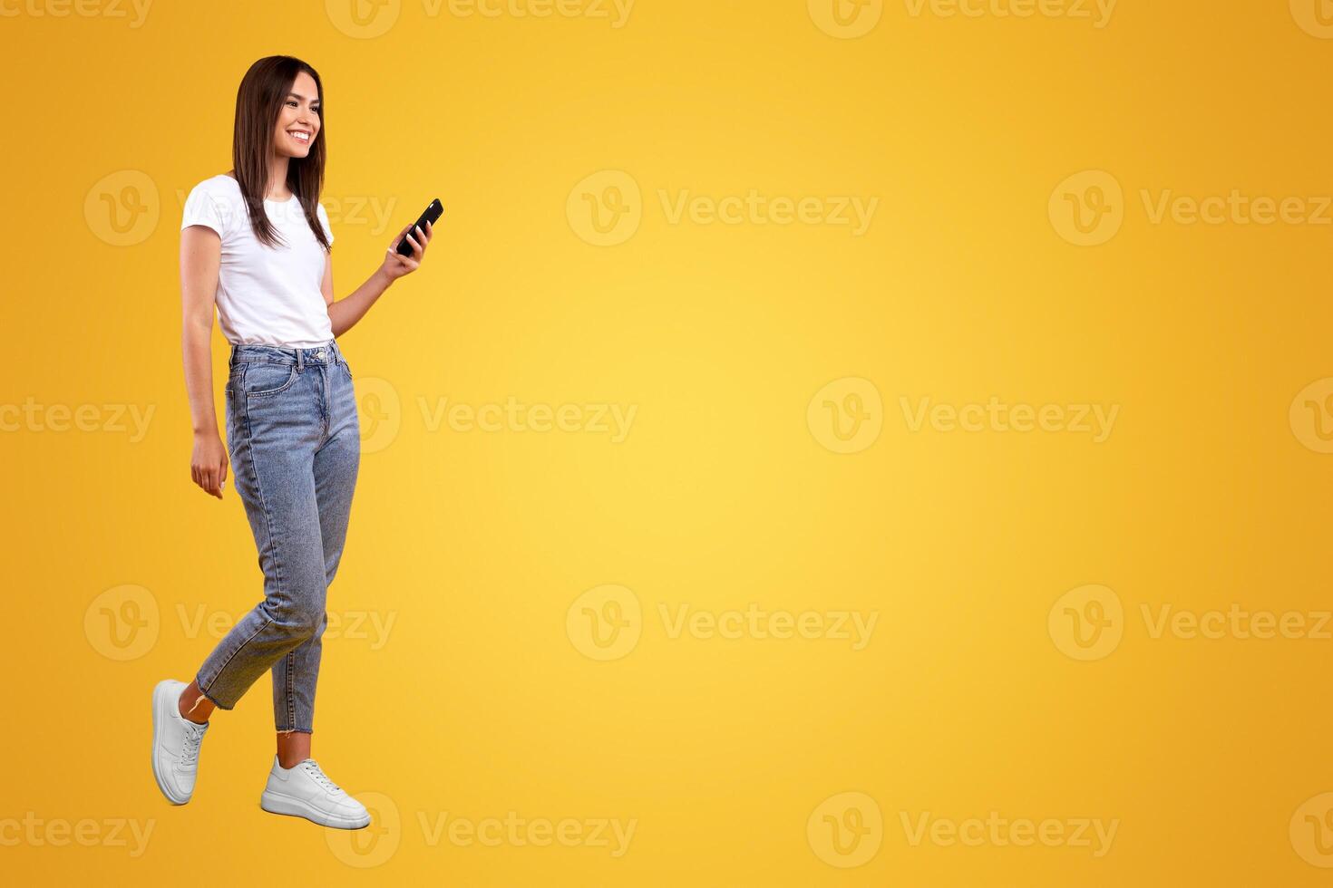 Communication, Technology And Lifestyle Concept. Full body length of smiling young lady using cell phone, walking isolated on orange studio background, profile side view panoramic banner, free space photo