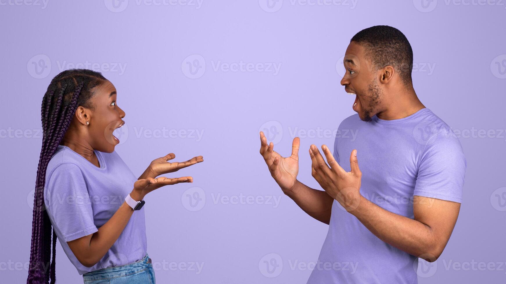 Omg, It's Unbelieveable. Portrait of exited amazed young black guy and lady looking at each other with open mouth. Emotional surprised couple standing isolated on purple violet studio background wall photo