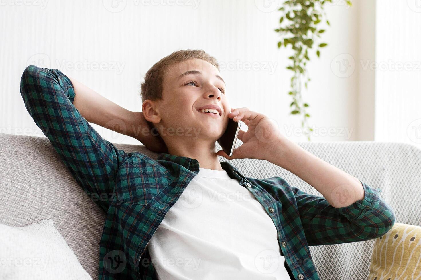 Relaxed teenager sitting on couch at home, talking on mobile phone, empty space photo