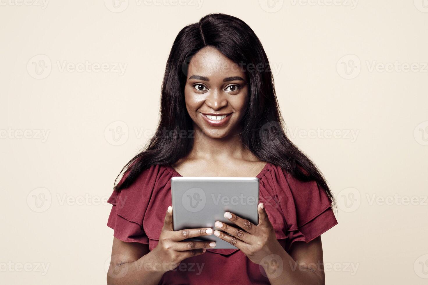 Cheerful african american young woman in casual outfit using brand new digital tablet, checking newest mobile application or playing online game, beige studio background, copy space photo