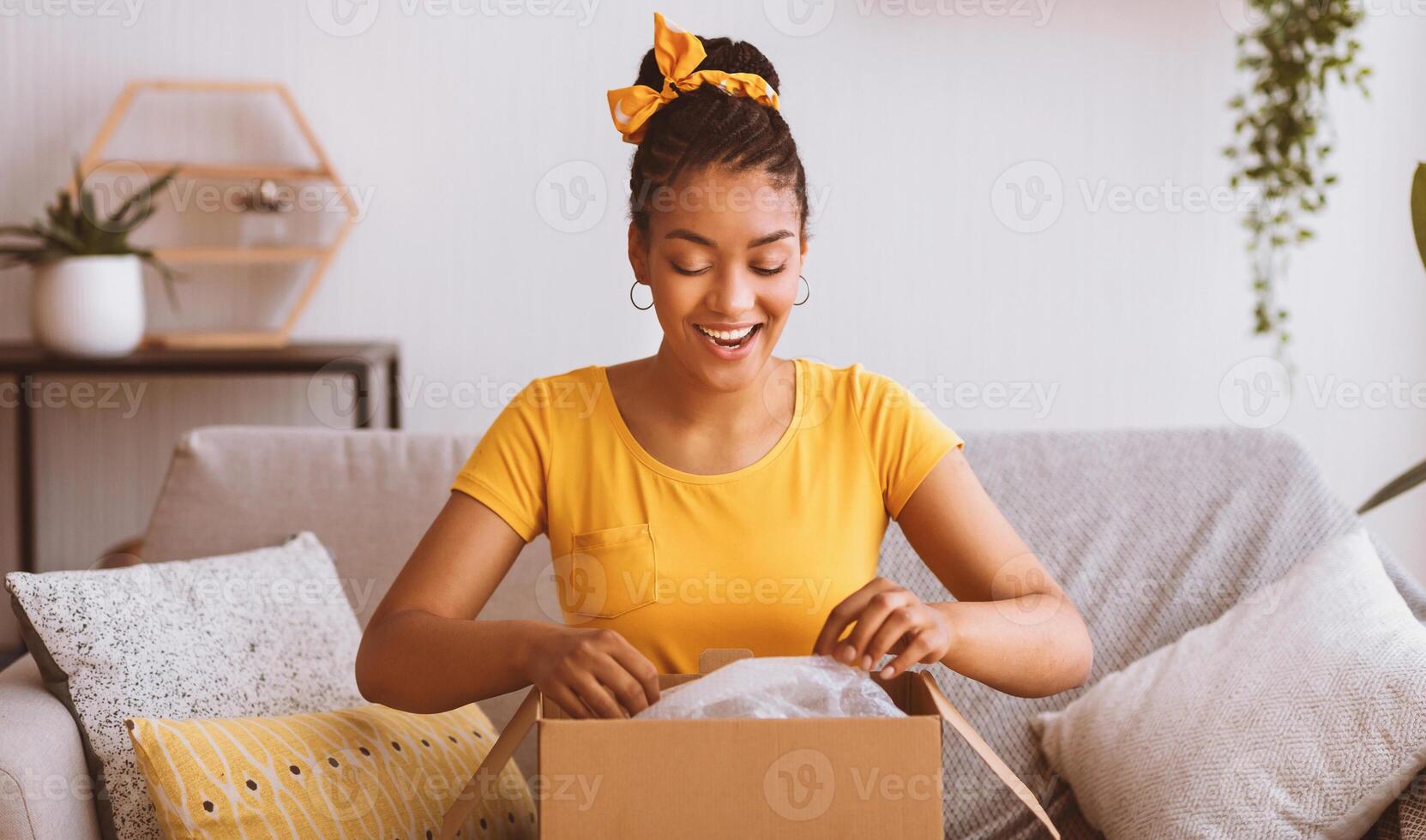 Quick Delivery Service Concept. Happy black lady received package, unpacking cardboard box, sitting on the sofa in living room at home, copy space. Female buyer satisfied with online shopping purchase photo