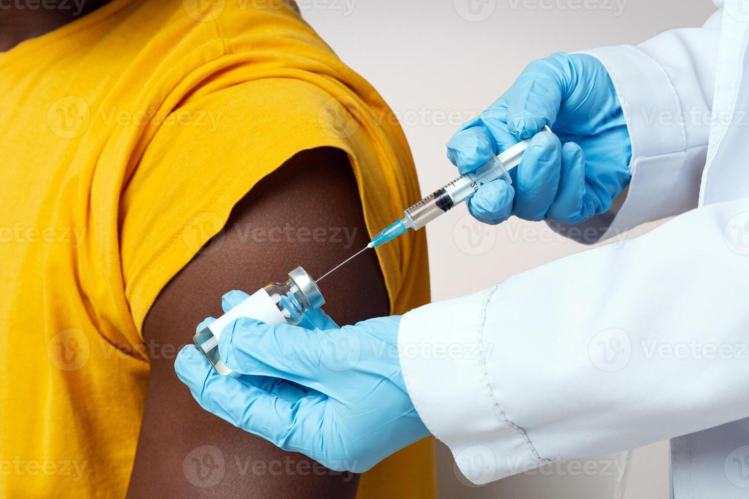 Unrecognizable Doctor With Syringe Taking Dose Of Vaccine From Vial, Ready To Make Injection To Young African American Man, Nurse Wearing Blue Latex Gloves Making Covid-19 Vaccination To Black Guy photo