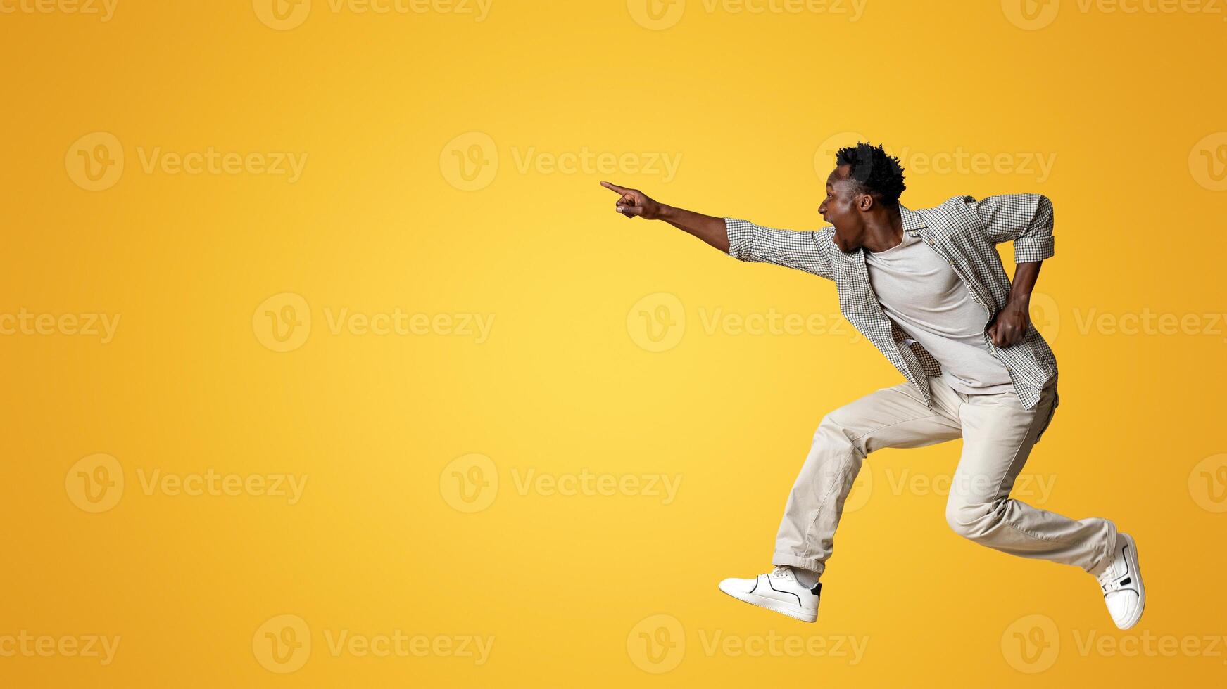 Crazy Sales. Emotional black man pointing aside while jumping in air over beige studio background, overjoyed excited african american guy showing copy space for design or advertisement, panorama photo