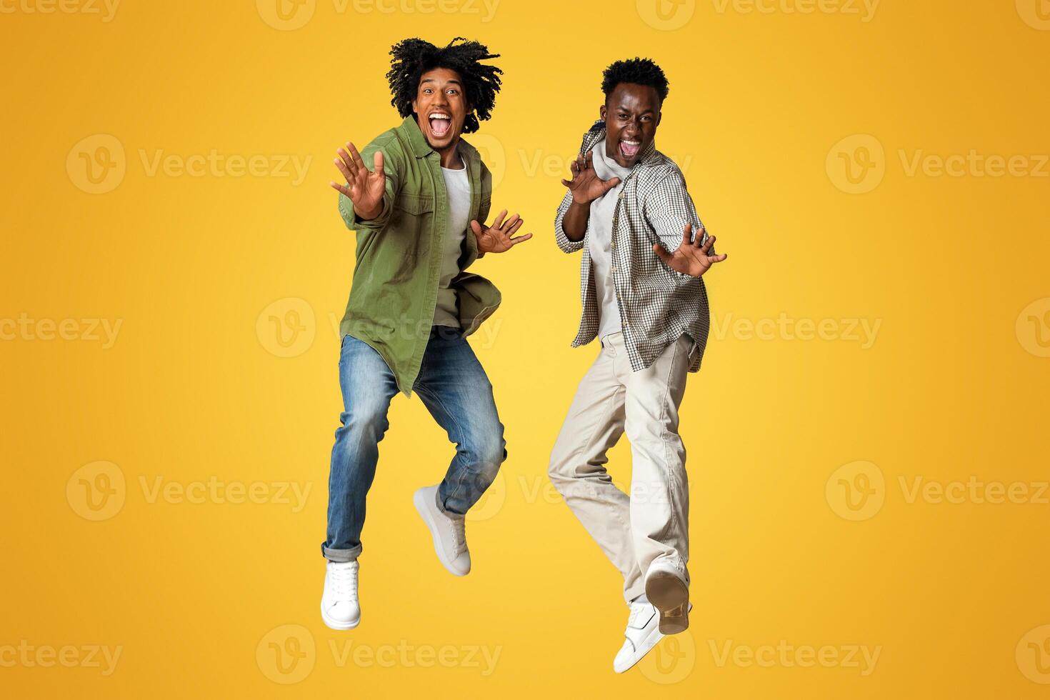 Two Cheerful Emotional African American Guys Jumping On Beige Studio Background, Full Length Shot Of Positive Crazy Black Male Friends Having Fun Together, Showing Karate Moves In Motion, Copy Space photo