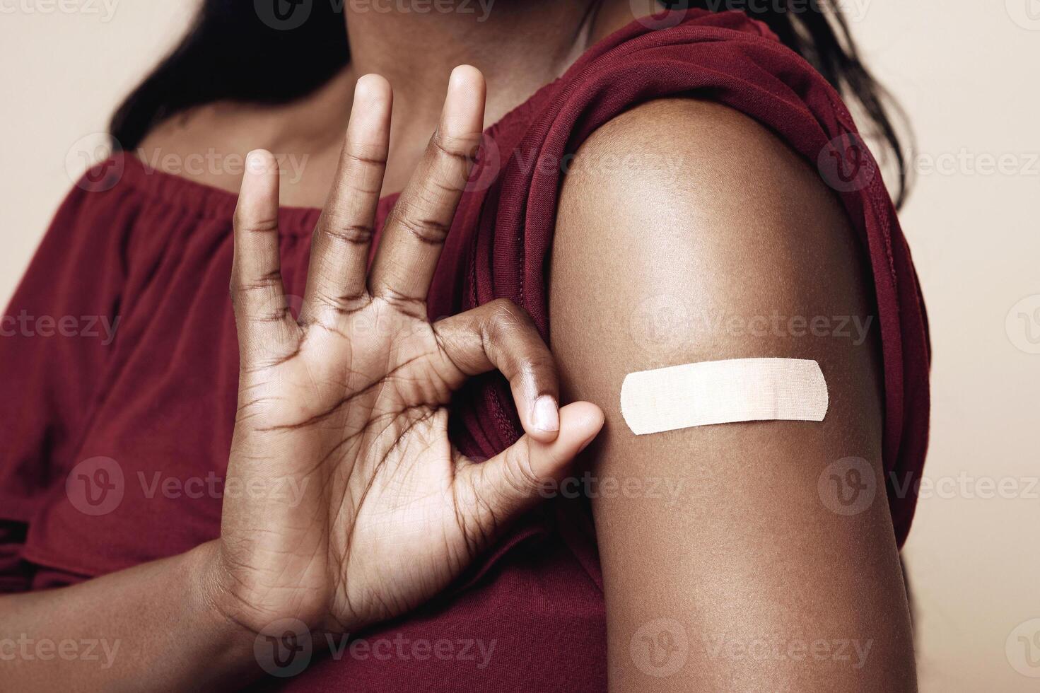 Safety immunization, vaccination against COVID-19 concept. Unrecognizable african american woman showing her shoulder with medical band on and okay gesture, recommending to vaccinate, closeup photo