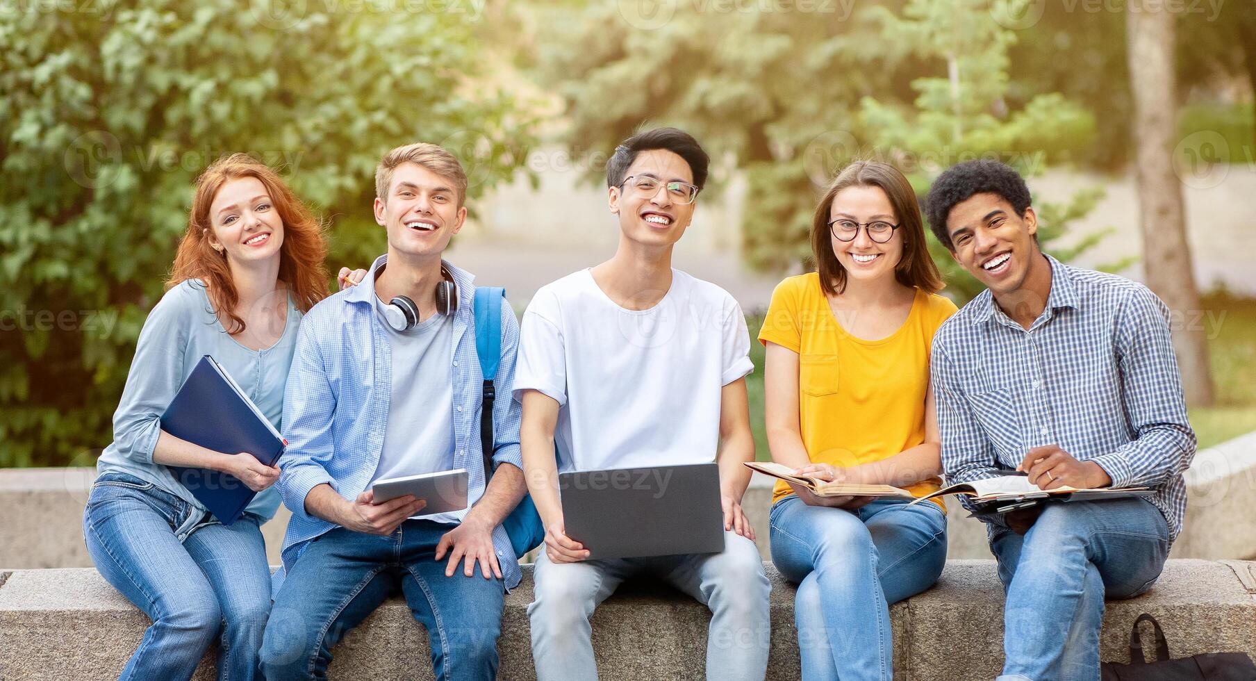 Happy Diverse Students Posing Sitting And Learning Together Using Laptop Computer Outside, Smiling To Camera. Education Concept photo