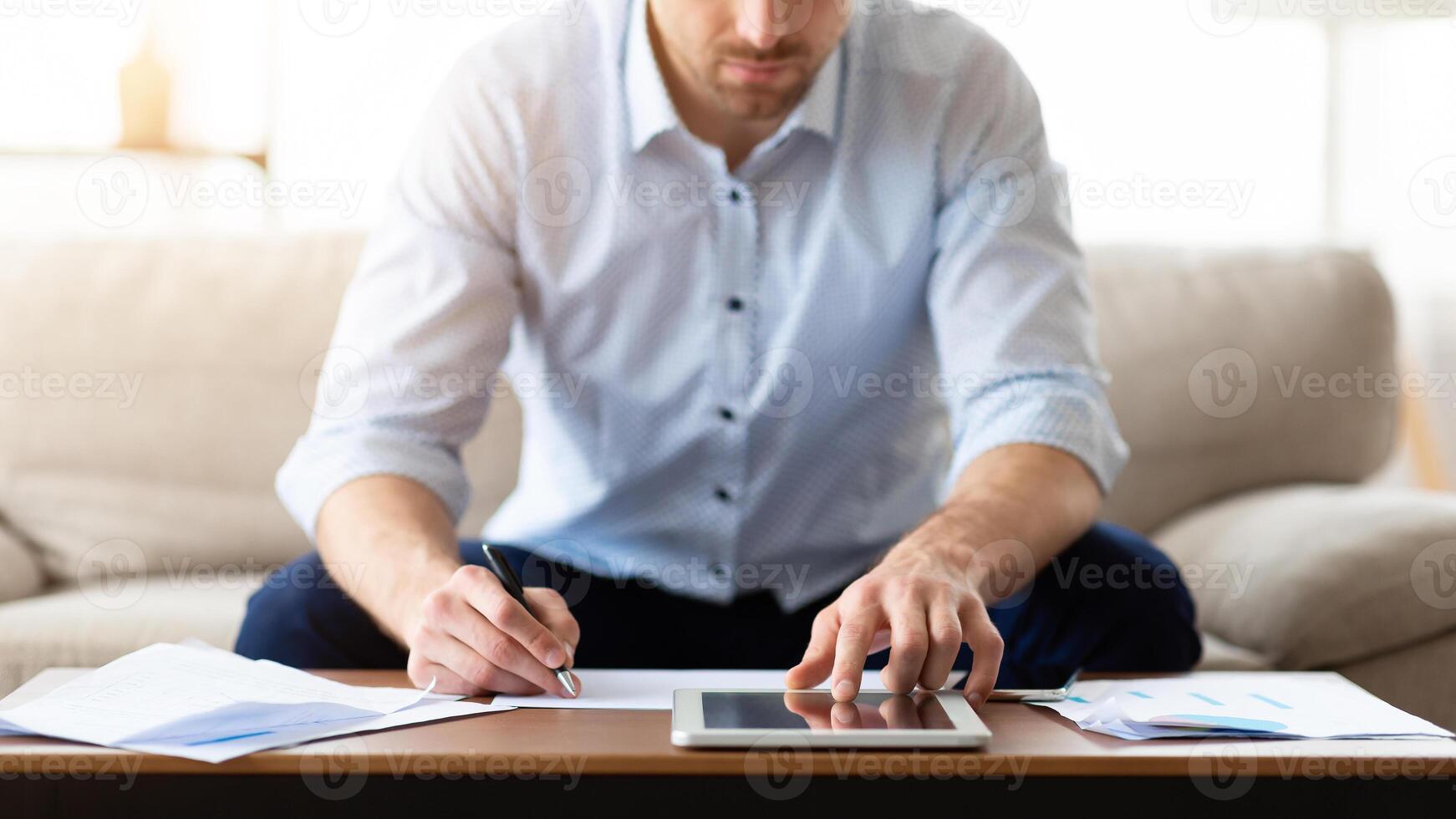 Budget Planning Concept. Pensive Man Using Tablet And Writing Sitting At Desk On Sofa At Home photo