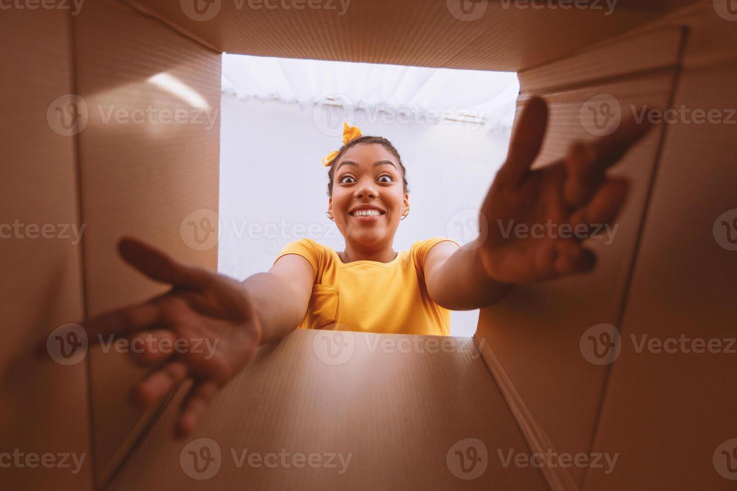 Delivery Concept. Excited african woman unpacking, opening carton box and trying to get something, view from the inside photo