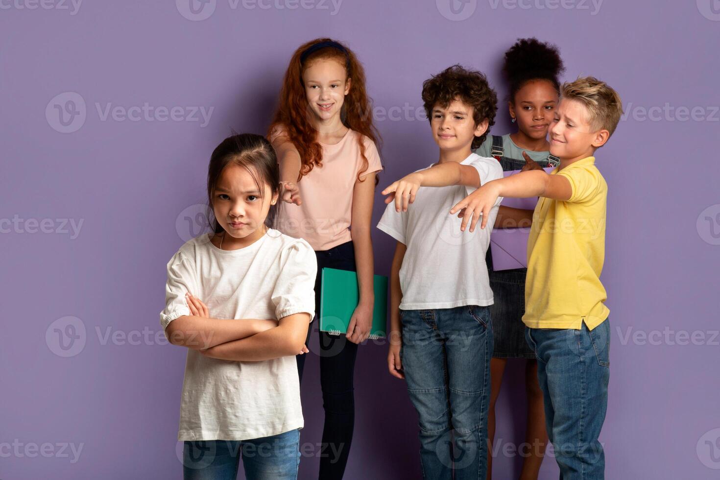 Stop bullying in schools. Upset Asian girl and her cruel classmates pointing at her over lilac background photo