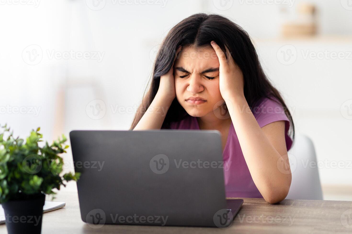 Exhausted Indian teen girl suffering from headache, having migraine, overworking, having too much online homework indoors. Tired adolescent facing difficulties studying remotely photo