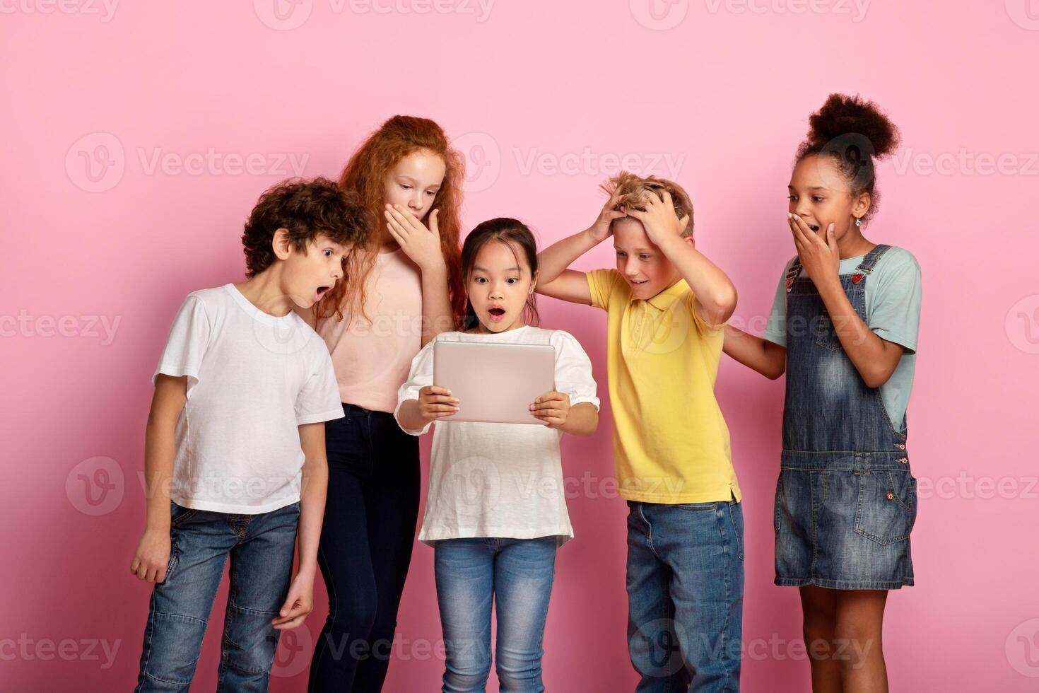 Group of shocked multiracial friends watching something on tablet computer together, pink background photo