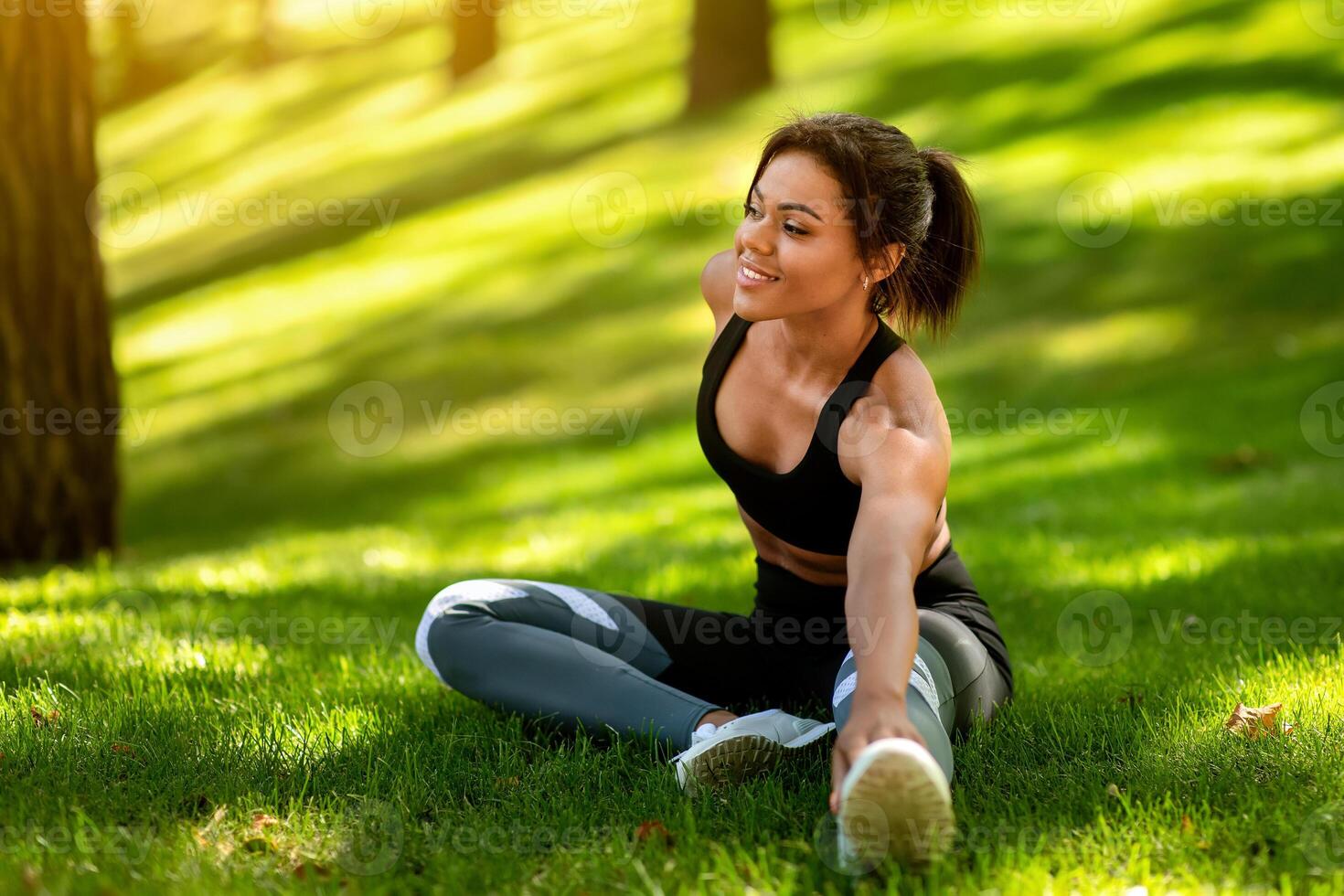 Healthy african woman warming up on the grass before jogging by park, free space photo