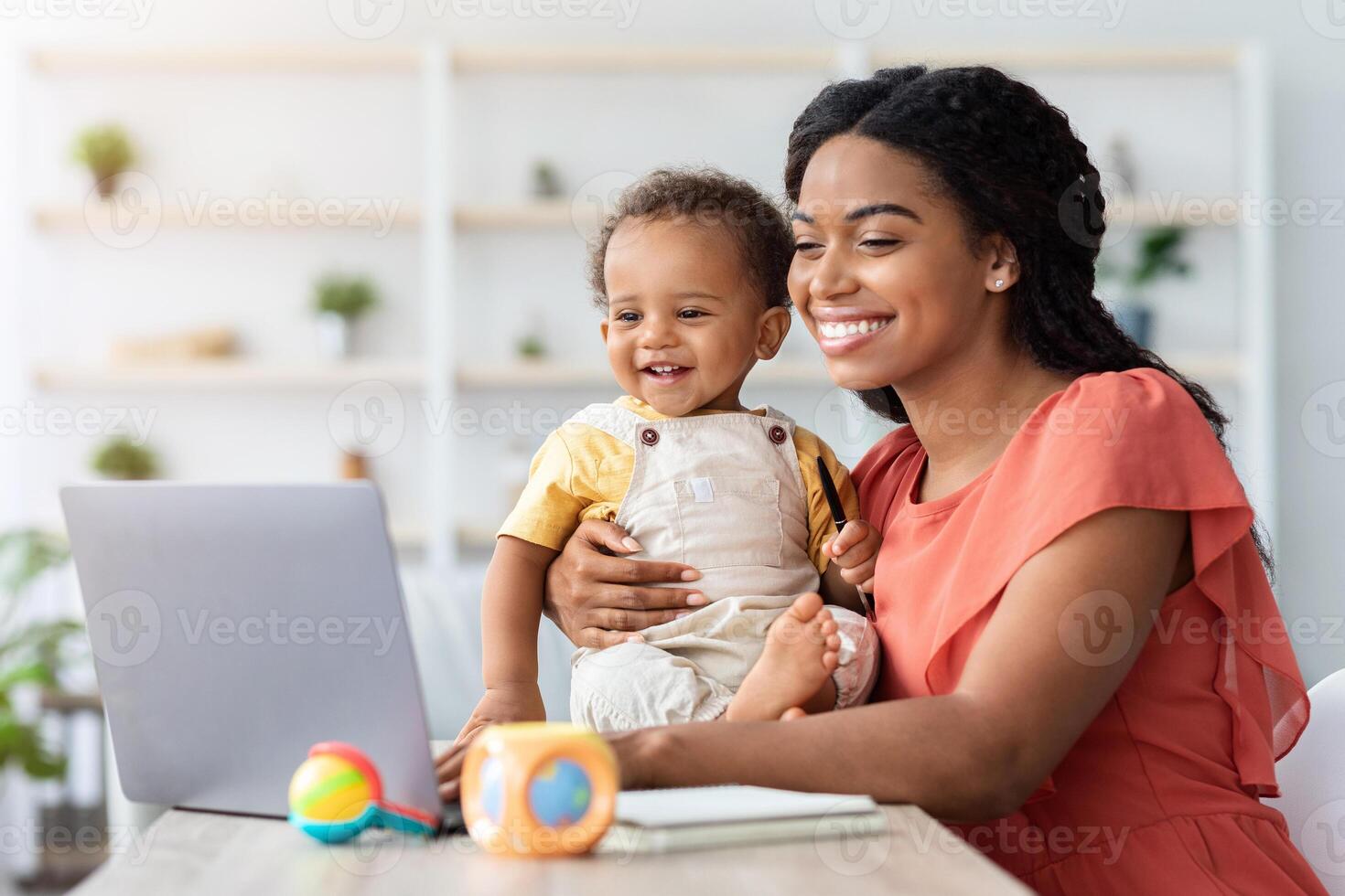 Happy Young Mom Working On Laptop And Taking Care About Baby At Home, Smiling African Lady Holding Cute Infant Son And Typing On Computer, Enjoying Remote Job During Maternity Leave, Free Space photo