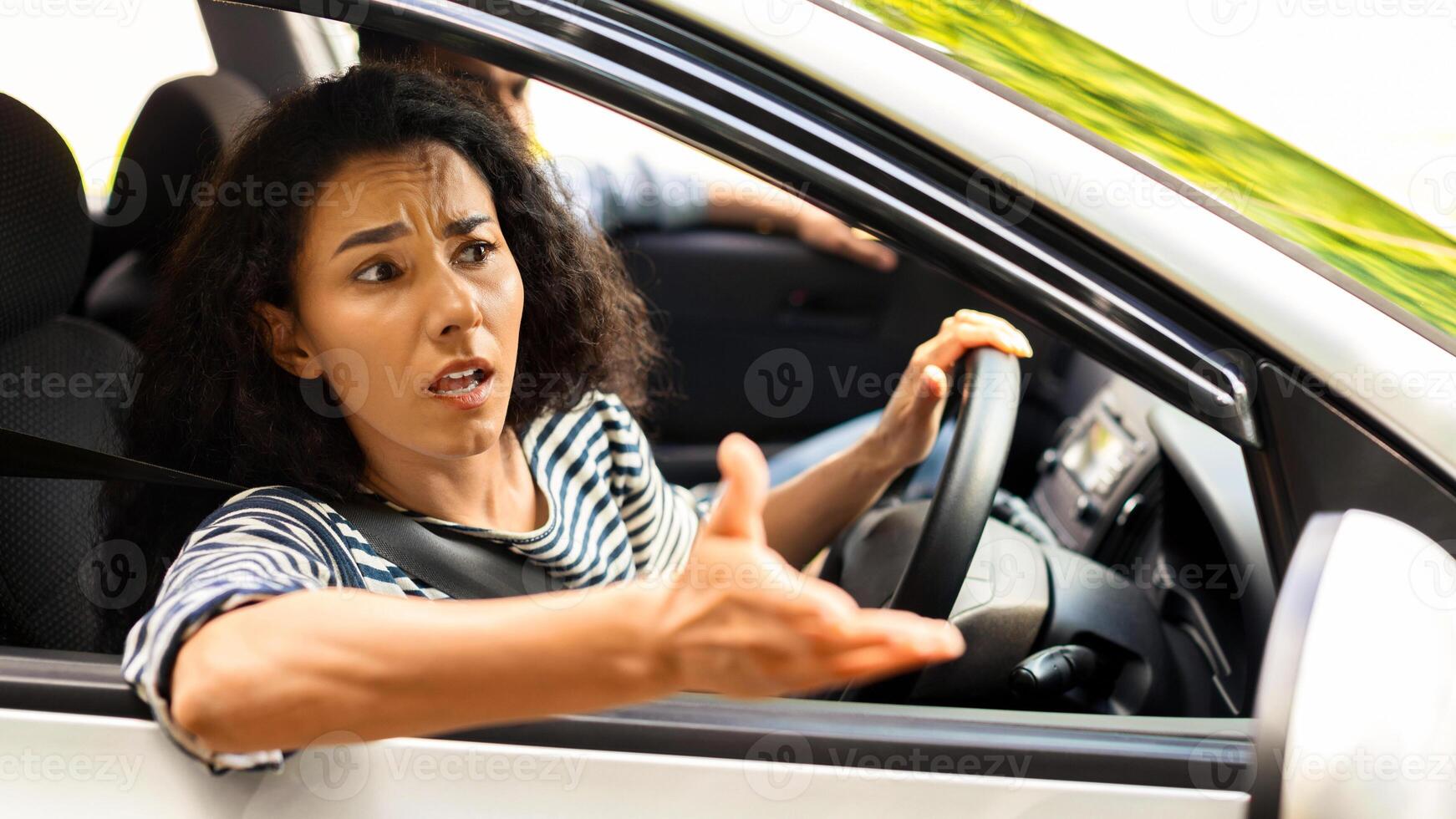 Indignant brunette lady driver fighting on the road, looking through car window, gesturing and yelling, woman got stuck in traffic or collided on the road, travelling with her boyfriend, side view photo