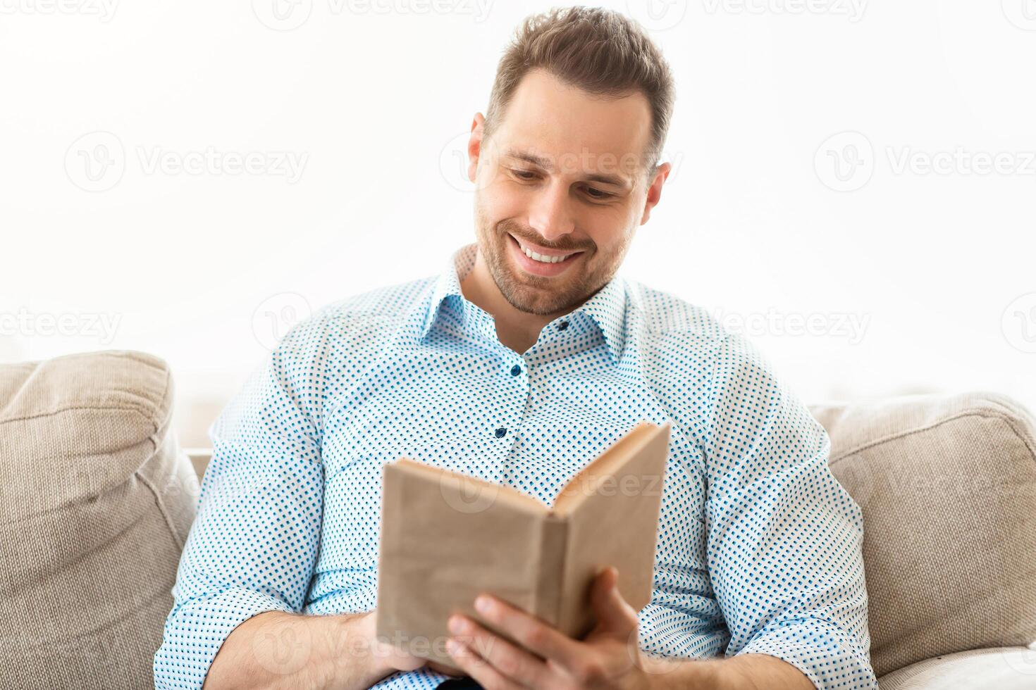 Time To Read. Smiling man holding paper book, resting on couch at home, copy space photo