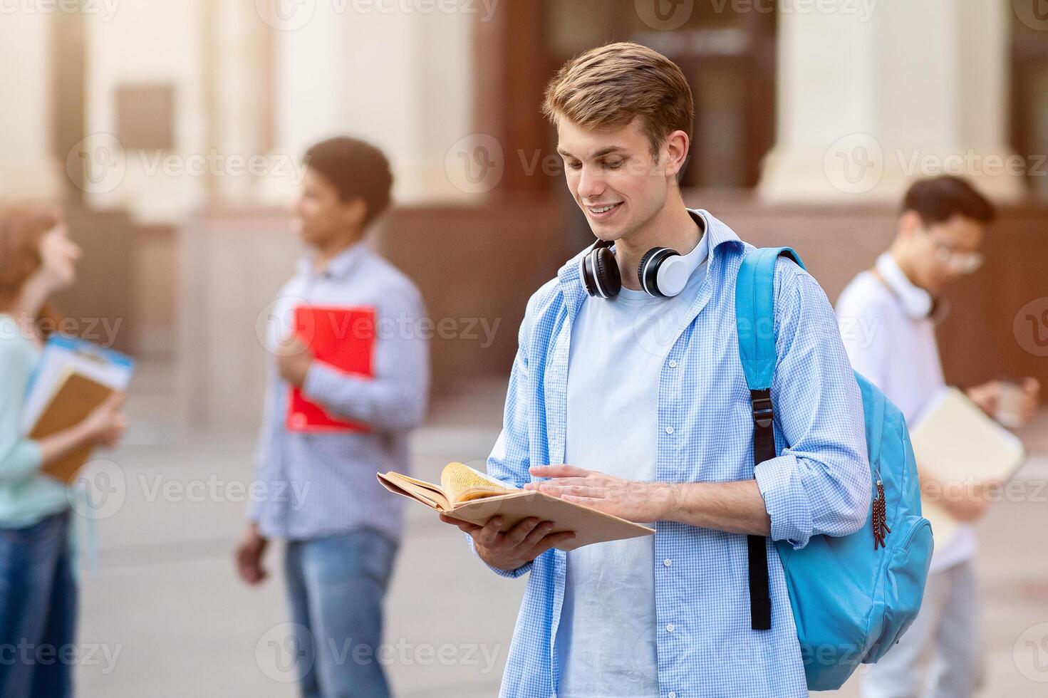 University Student Guy Reading Book Learning Standing Outside College Building. Getting Degree, Higher Education Concept photo