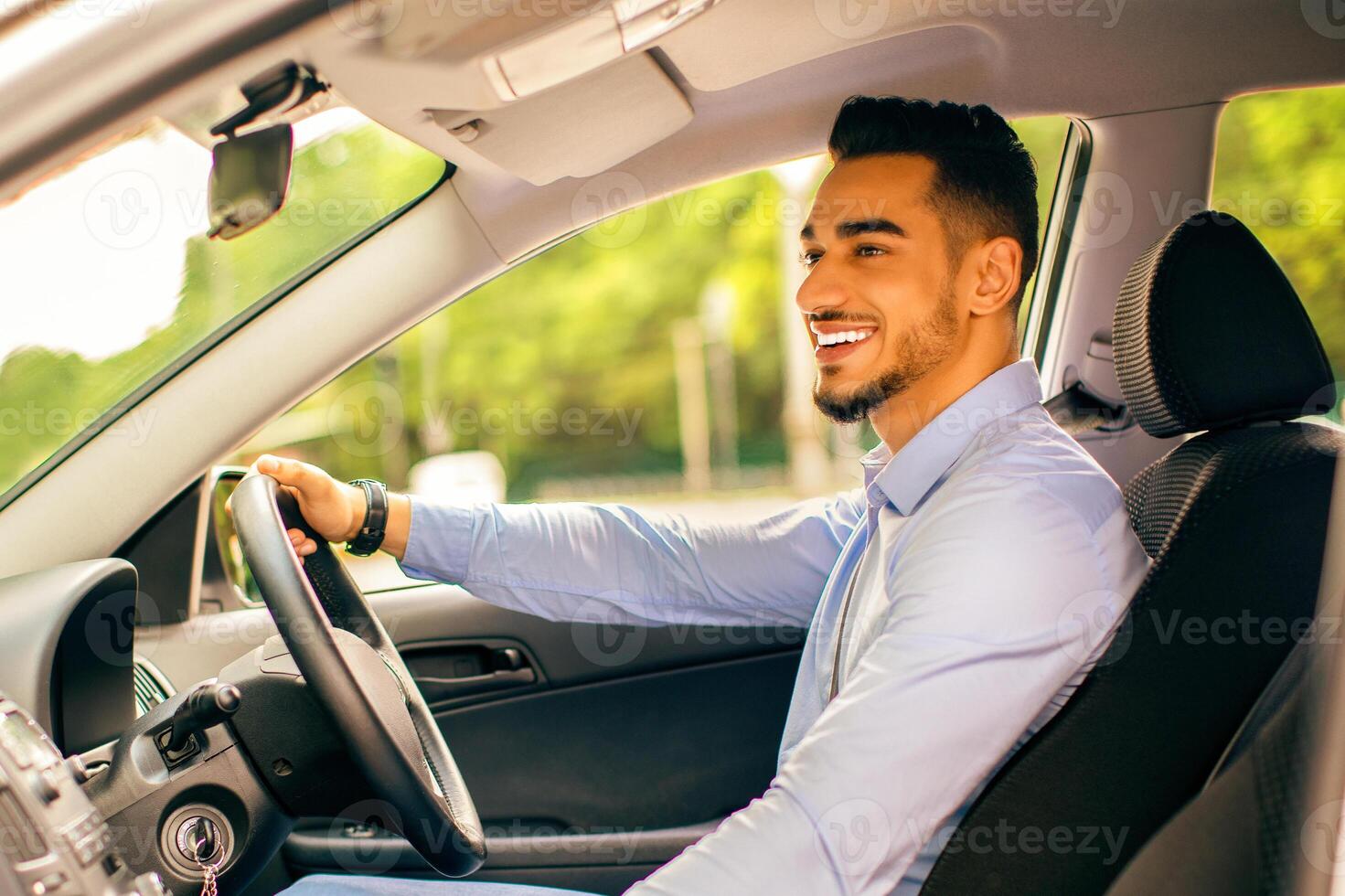 Cheerful arab businessman driving nice car, young middle-eastern manager or entrepreneur goign to job or business meeting, looking at road and smiling, copy space, side view. Business auto concept photo